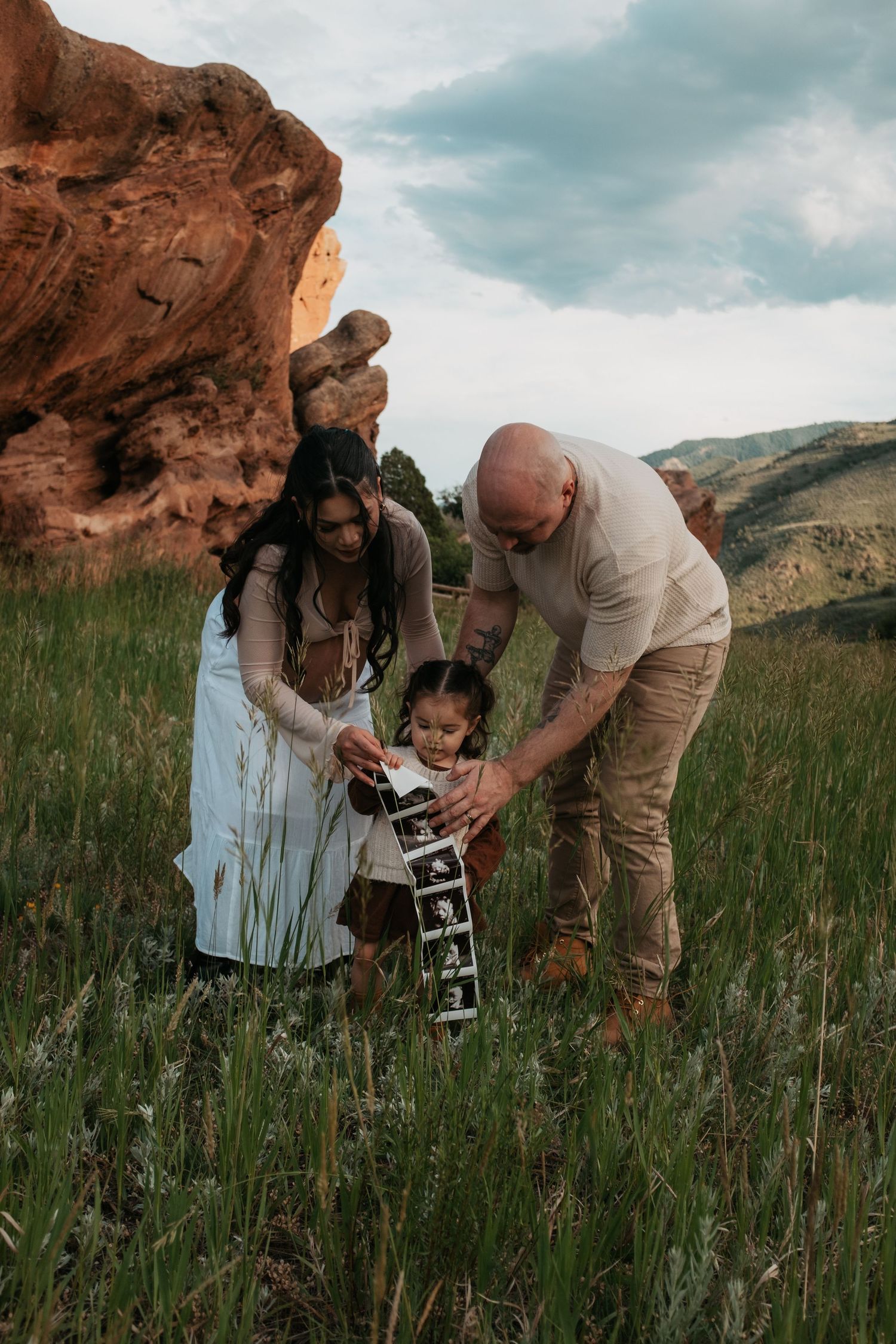 A family holds up a strip of ultrasound photos together in a scenic mountainous setting.