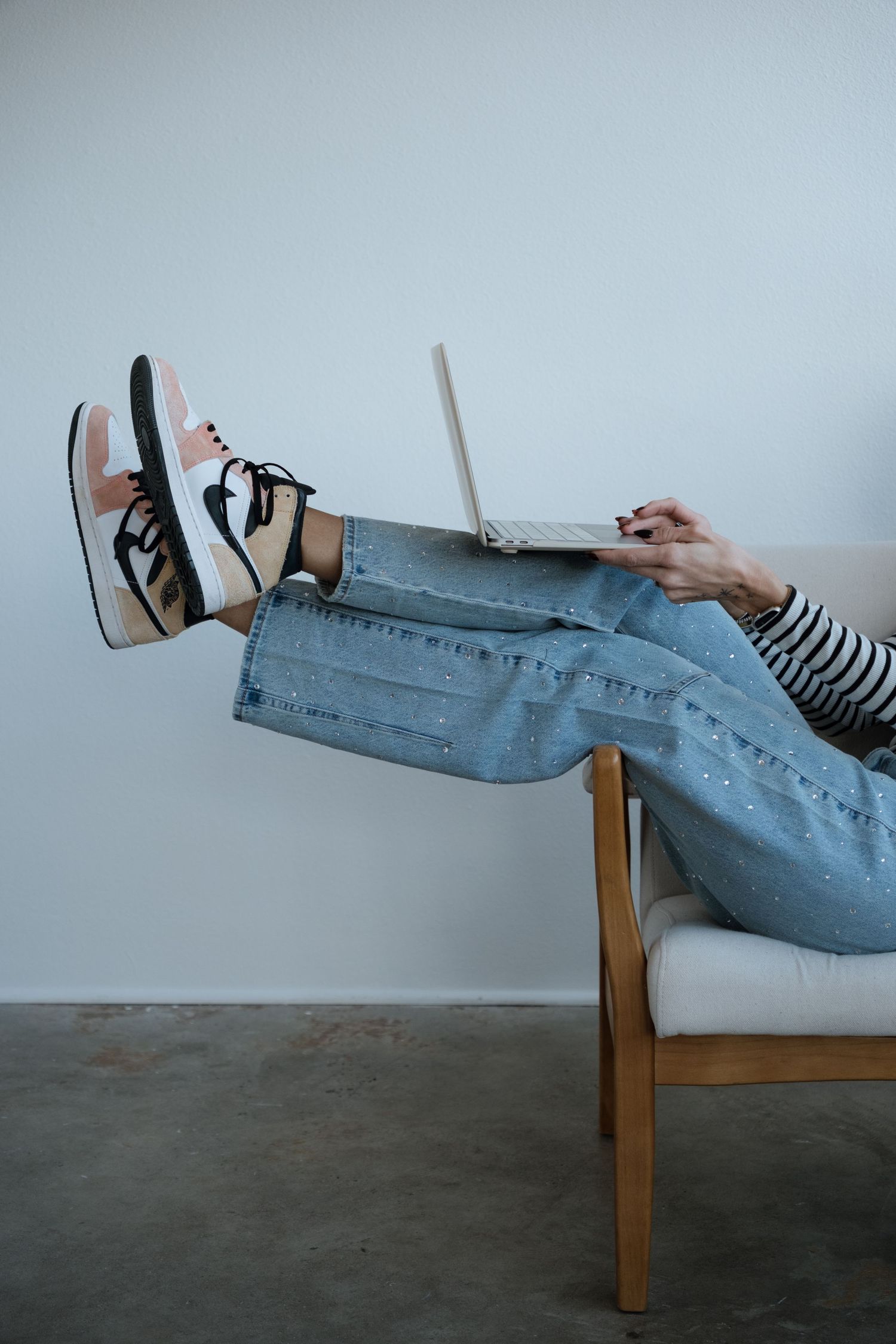 Person in jeans and sneakers relaxing on a chair while using a laptop computer.