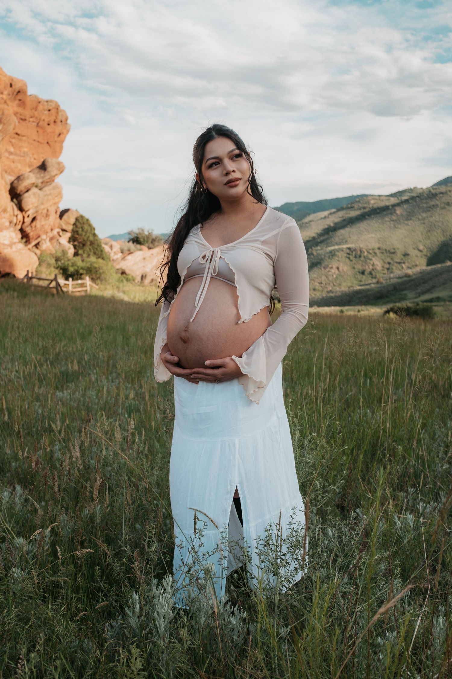 Ethereal maternity portrait in white dress amidst natural mountain scenery.