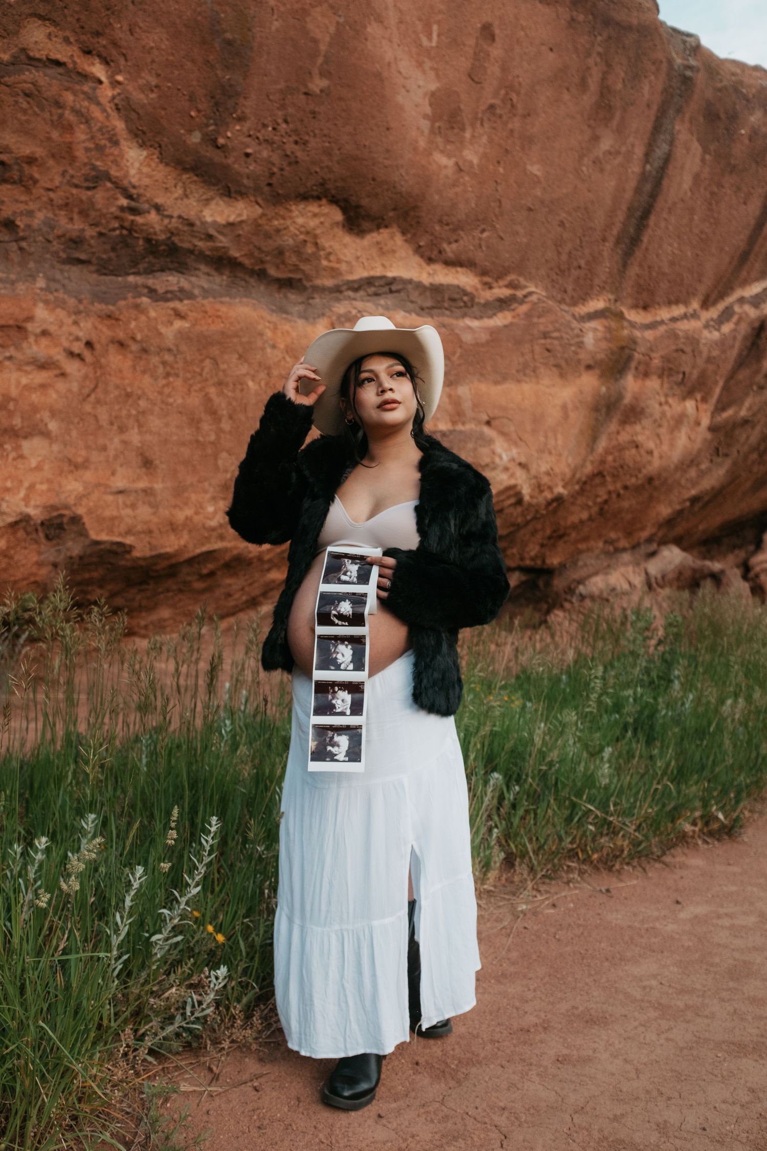 Maternity photo session featuring ultrasound prints against rustic red rock backdrop.