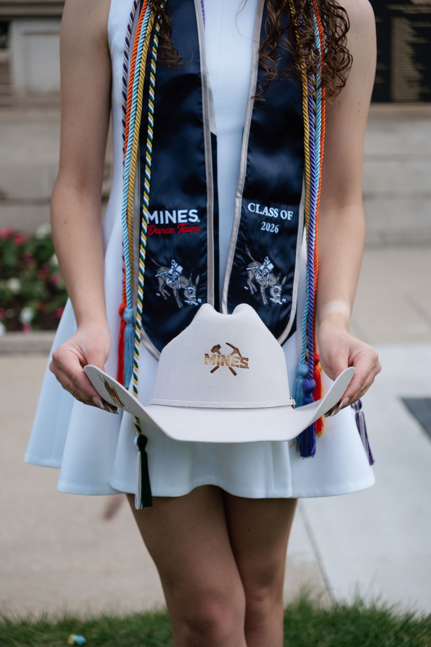 Colorado School of Mines Class of 2026 graduate holding white cowboy hat with colorful honor cords and navy stole.