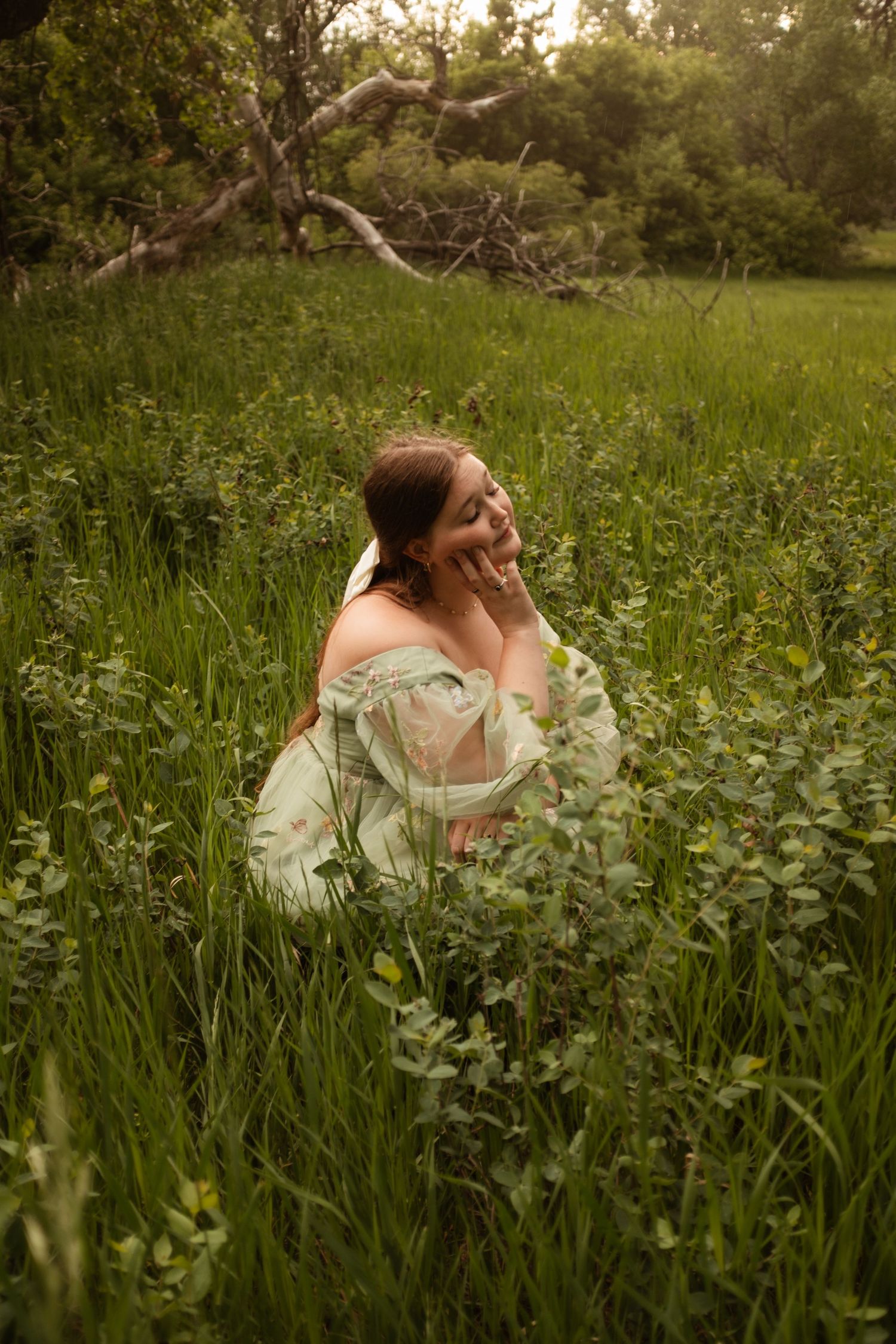 Someone wearing a flowy white dress poses gracefully among tall grass and wildflowers.