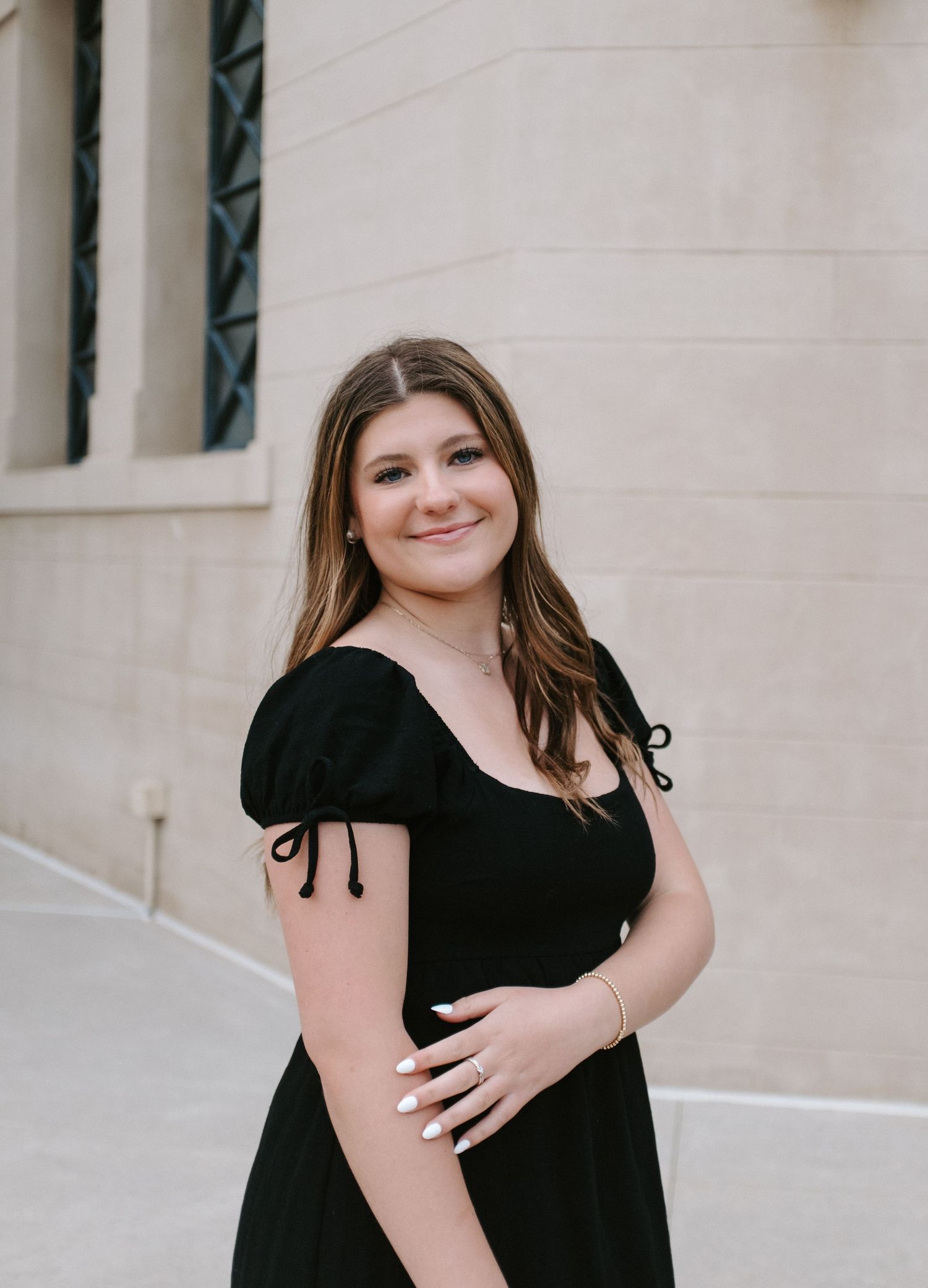 Portrait series in black dress against light colored building wall.