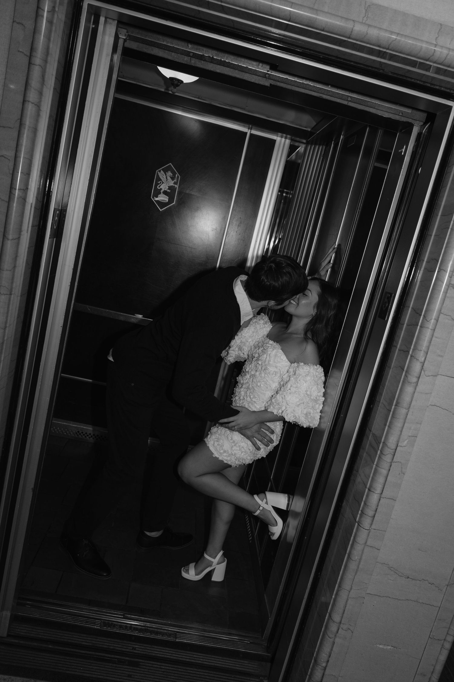 A black and white photo sequence showing a couple embracing and kissing in an elevator doorway.