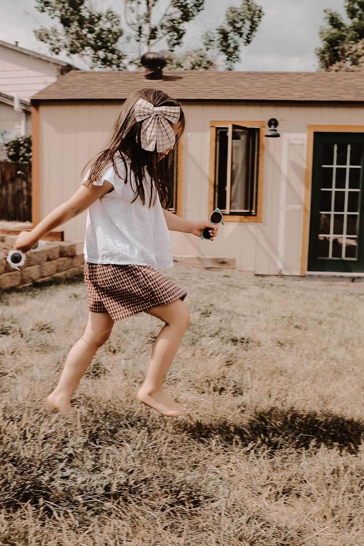 A playful moment captured in a backyard as someone runs carefree in a white top and plaid skirt.