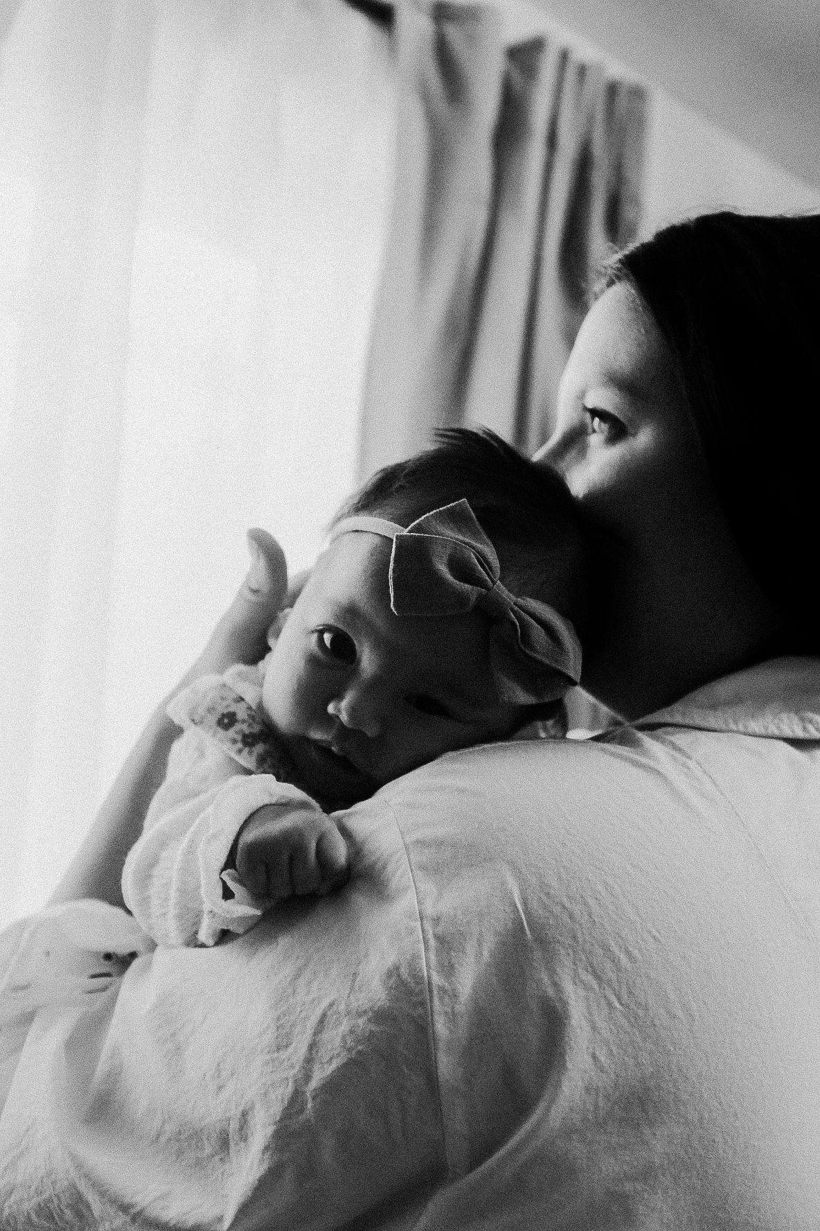 A tender black and white portrait of a parent and baby with a bow.