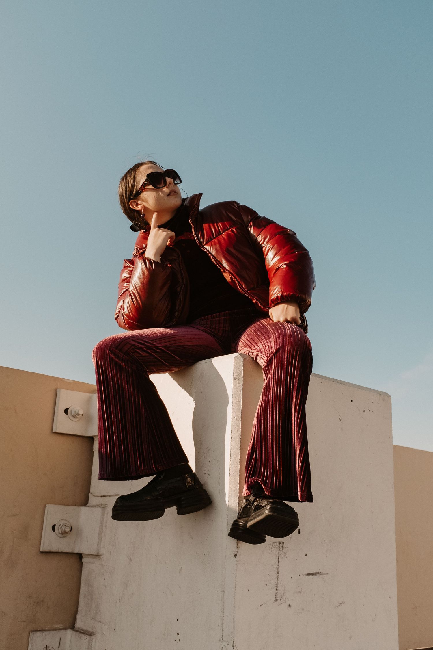 Person in red outfit sits contemplatively on concrete structure against blue sky.