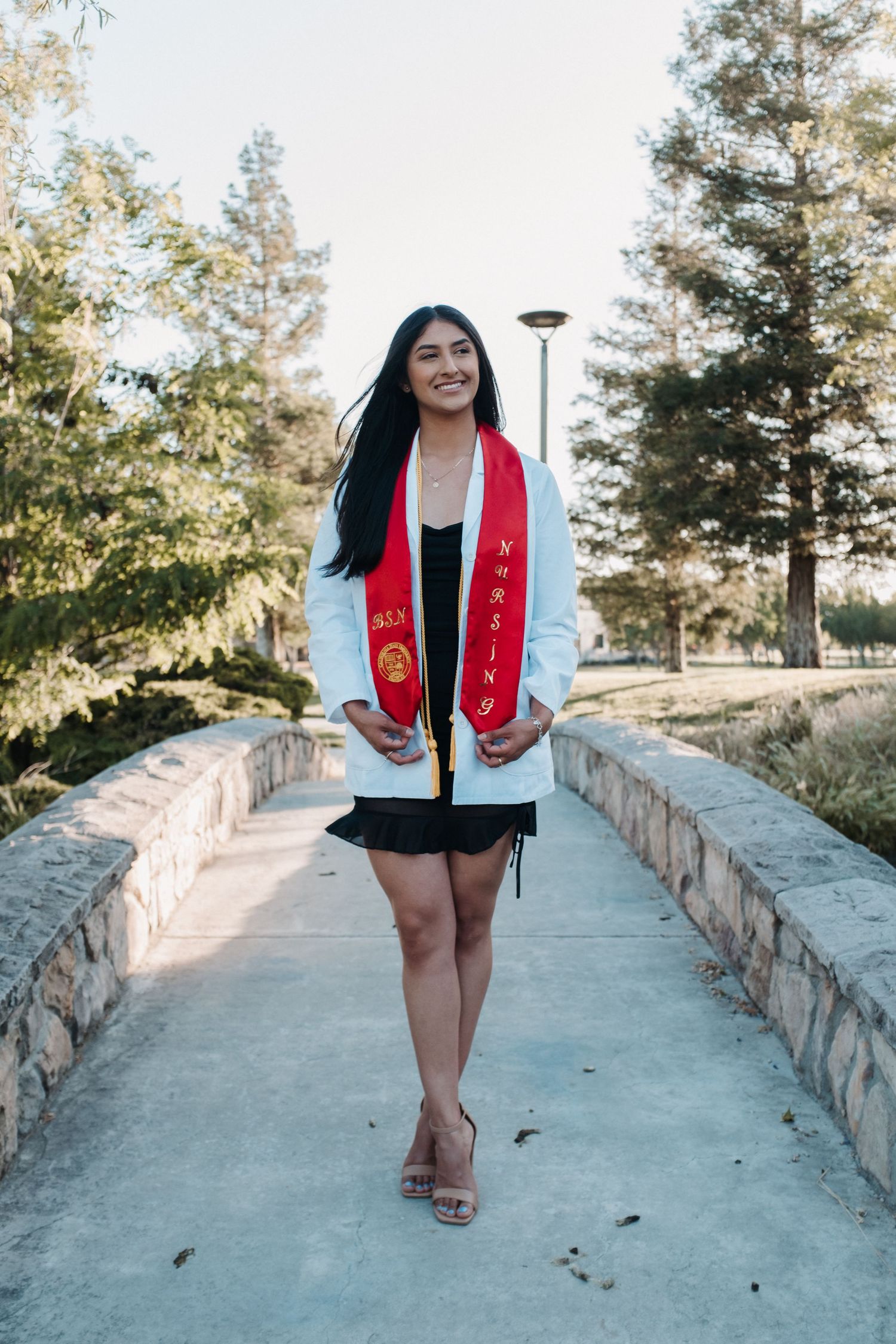 Graduate in white coat and red stole standing on stone pathway.