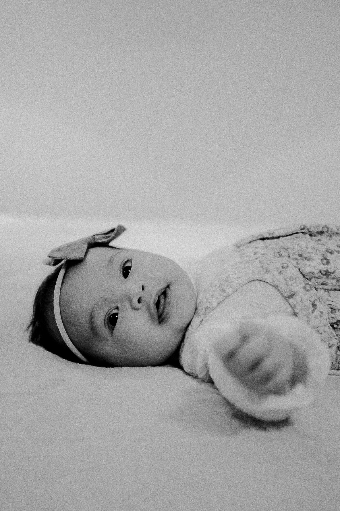 Black and white portrait of a baby lying down with a bow headband.