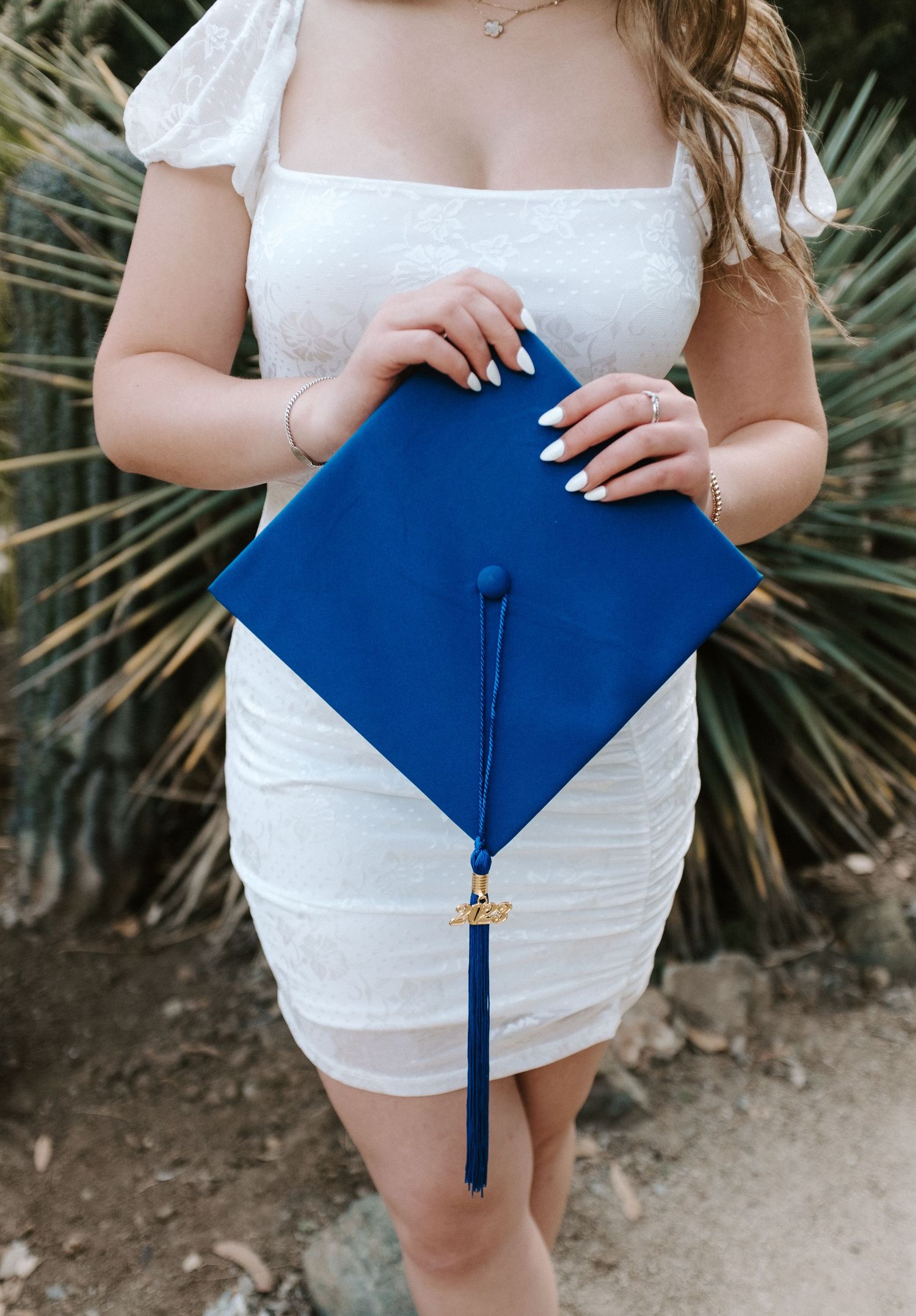 A close-up of someone holding a bright blue graduation cap against a white dress.