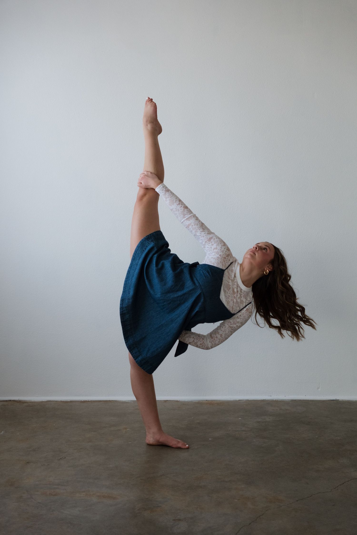 A barefoot dancer balances on one leg, extending the other high overhead in a graceful arabesque pose.