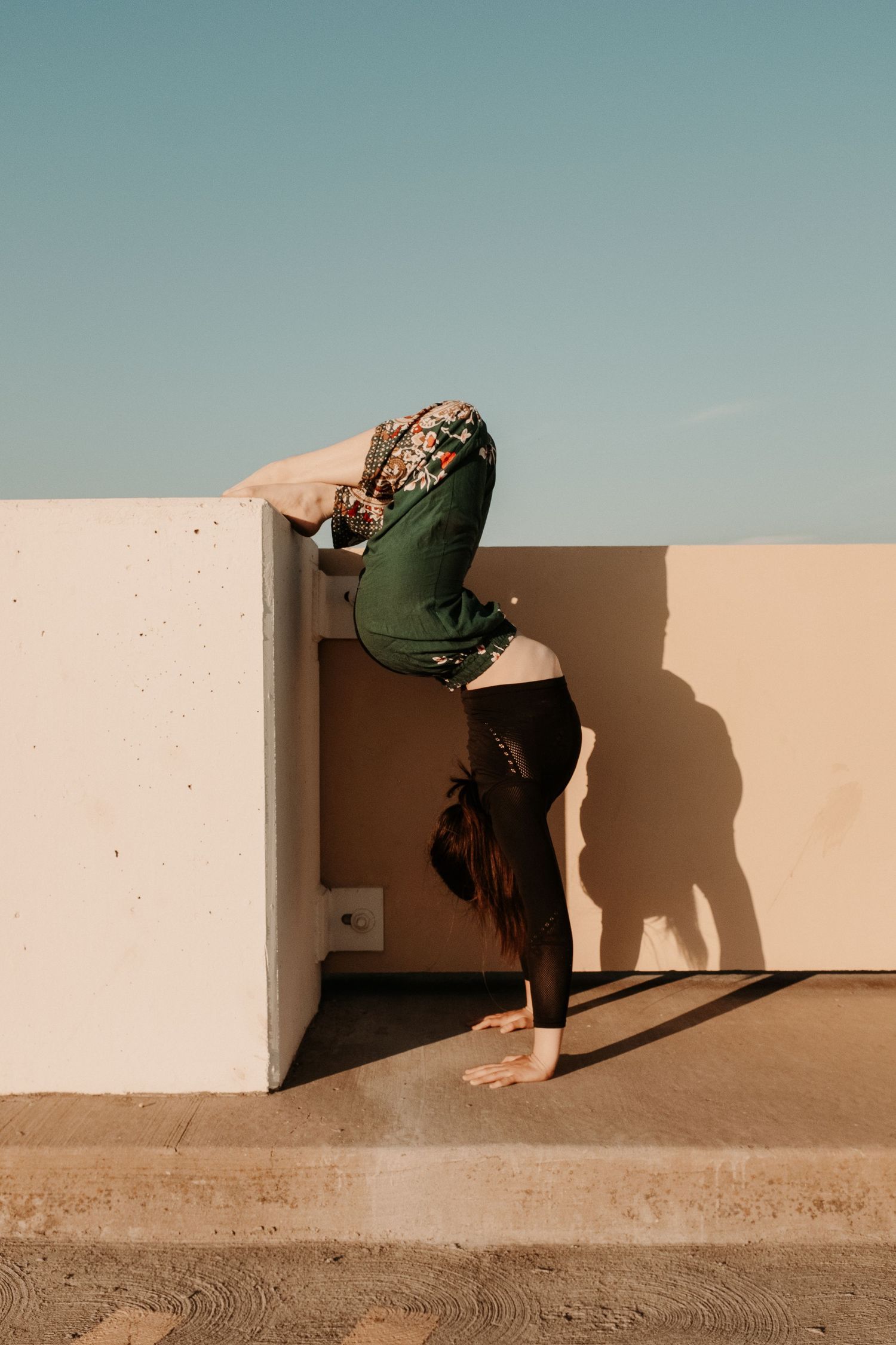 Creative dance pose against a wall creating dramatic shadows in natural light.