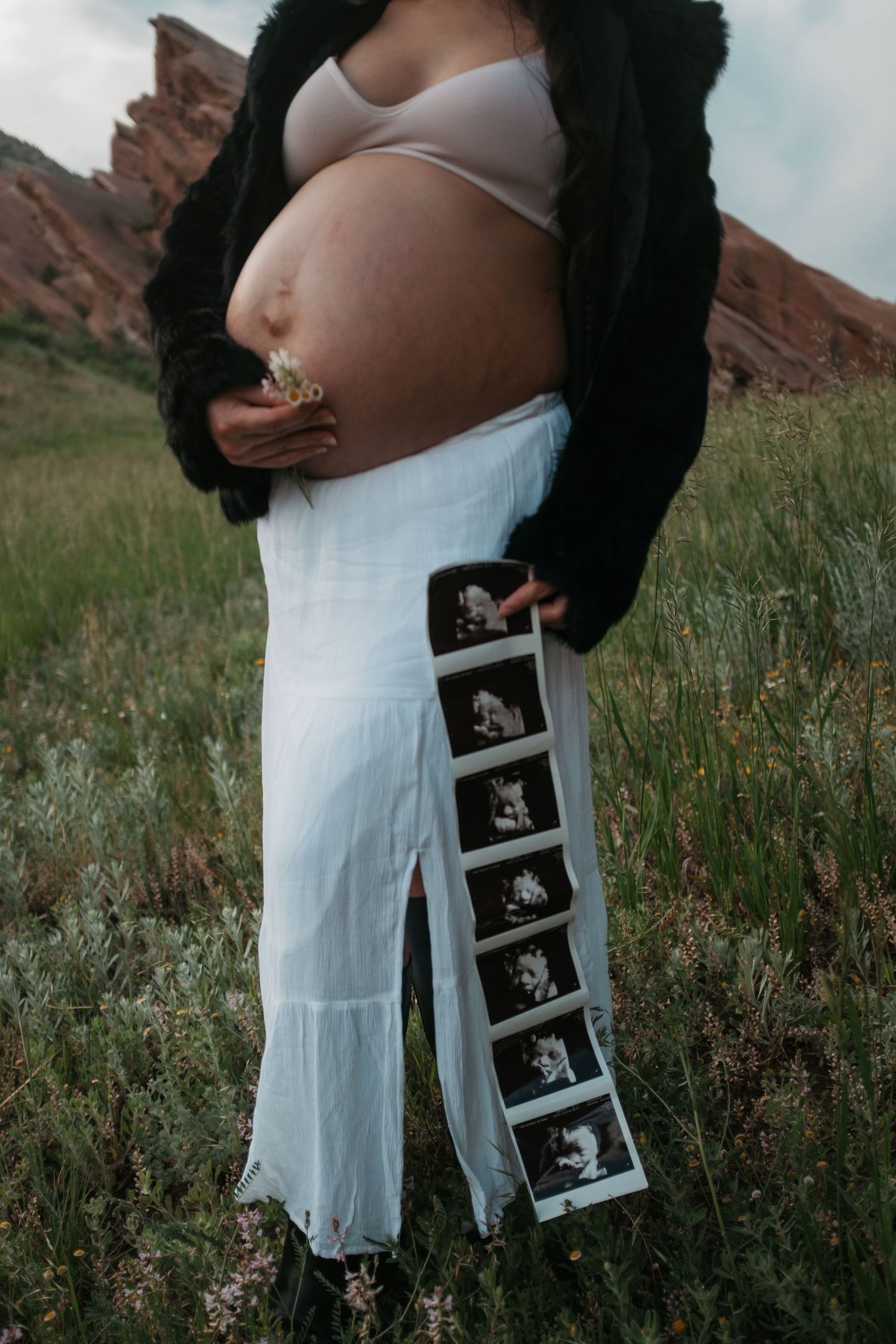 A pregnant belly with ultrasound photos arranged in sequence against a rocky outdoor backdrop.