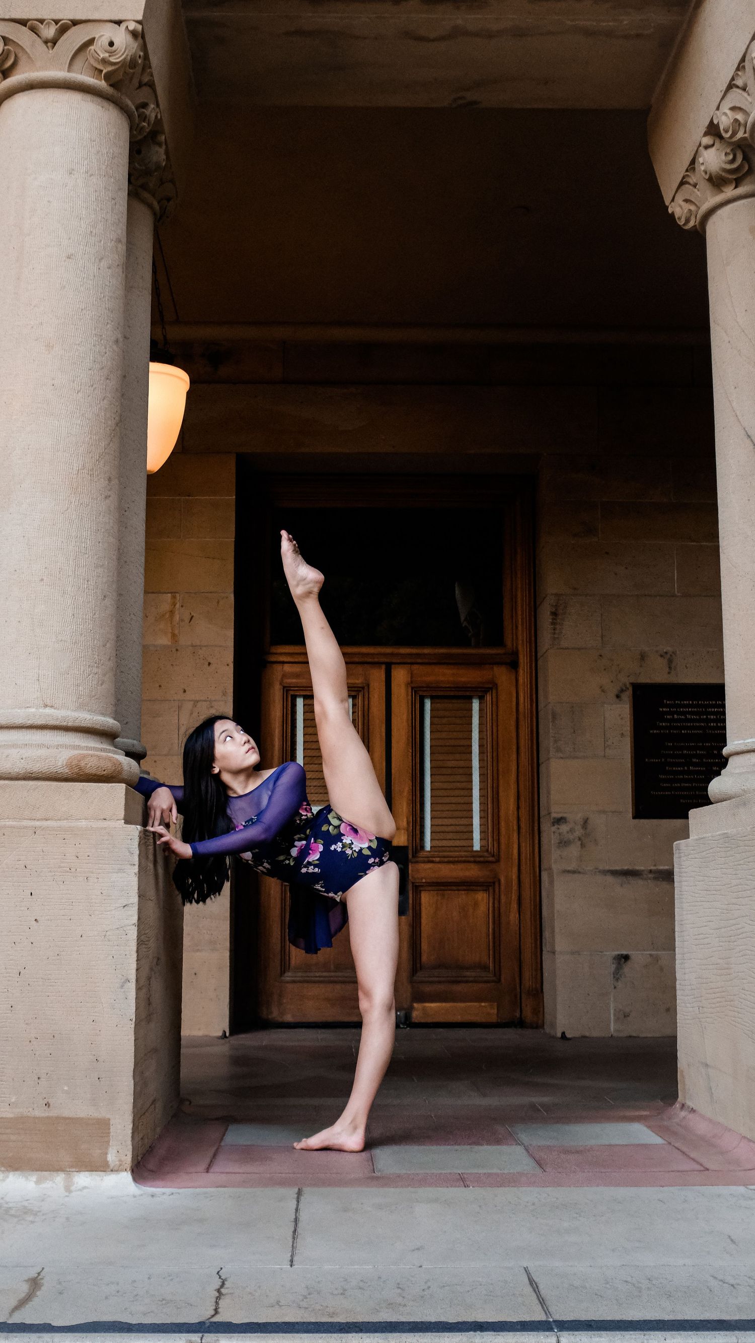 Ballet dancer performs graceful high kick sequence in historic stone colonnade.