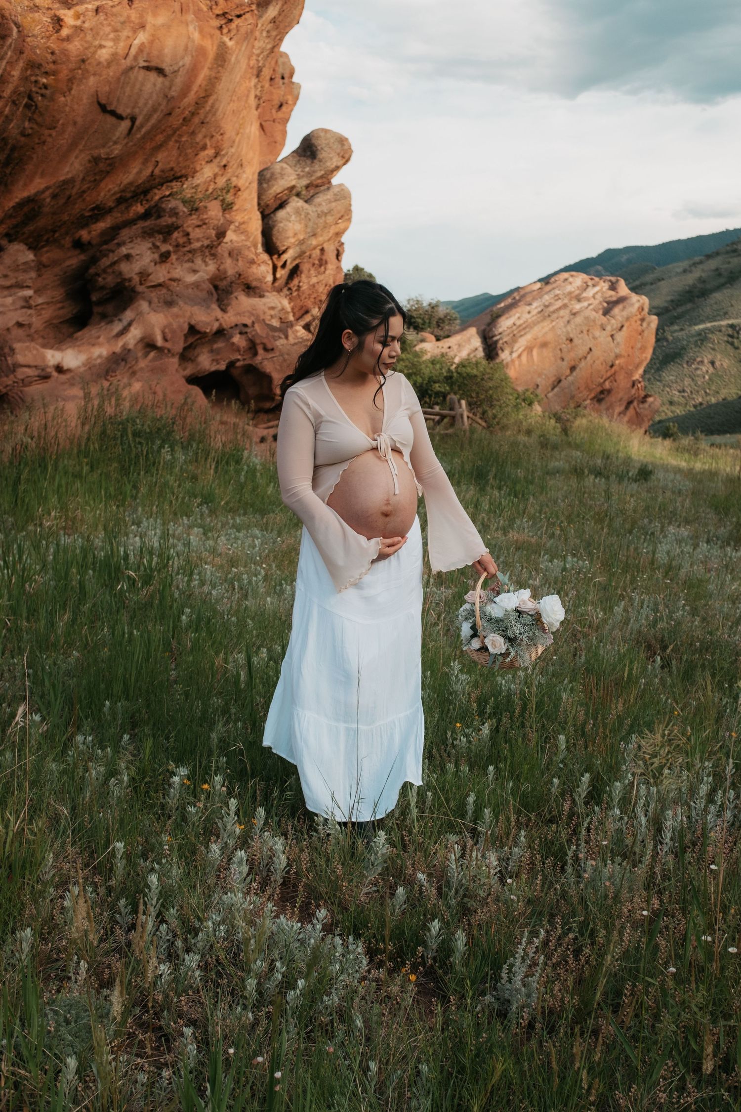 A peaceful maternity portrait taken in a meadow with dramatic red rock formations in the background.