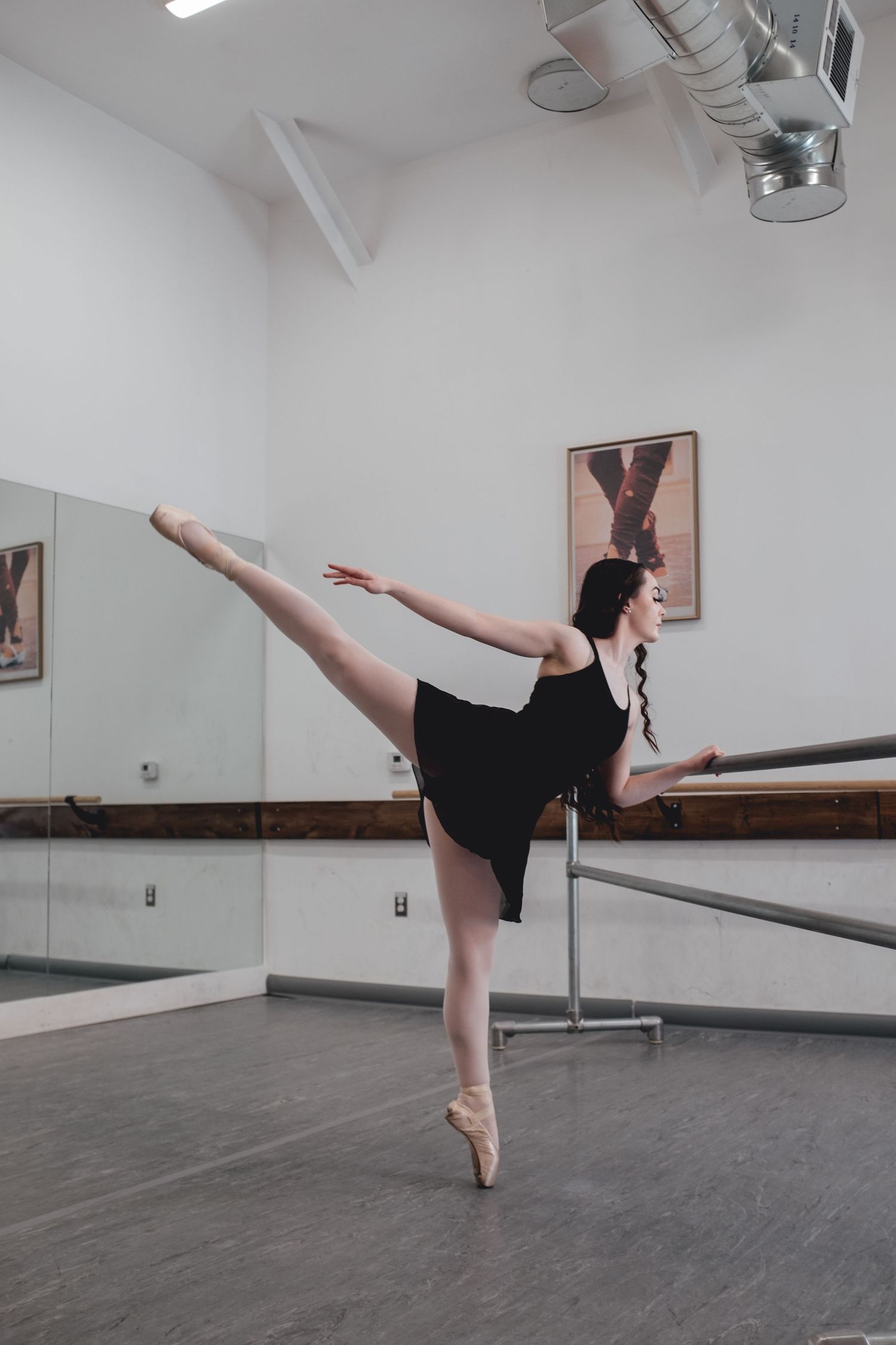 Ballet dancer executes arabesque position in white studio with wooden barre.