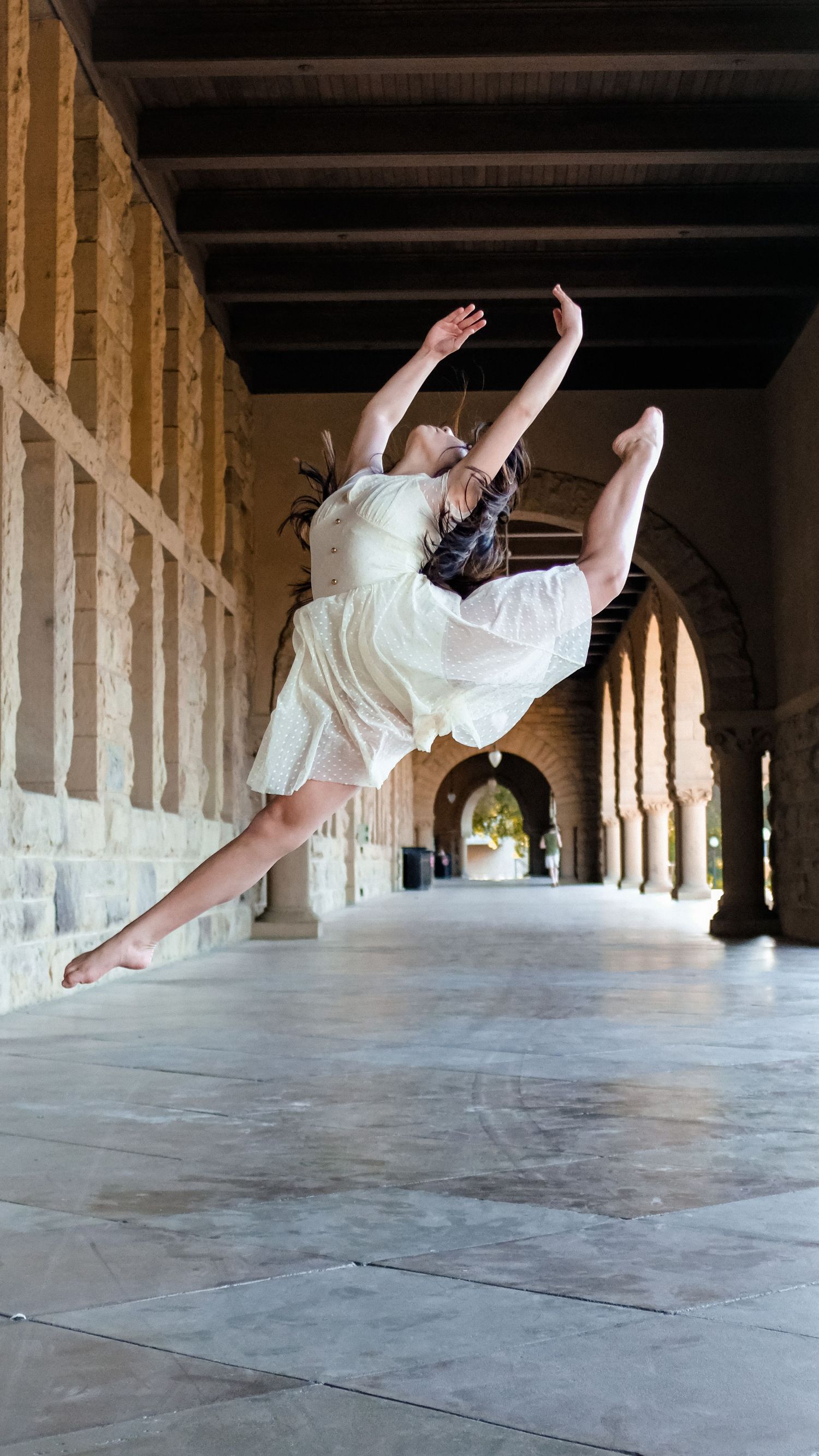 Dancer performs dramatic leap in historic stone archway corridor.