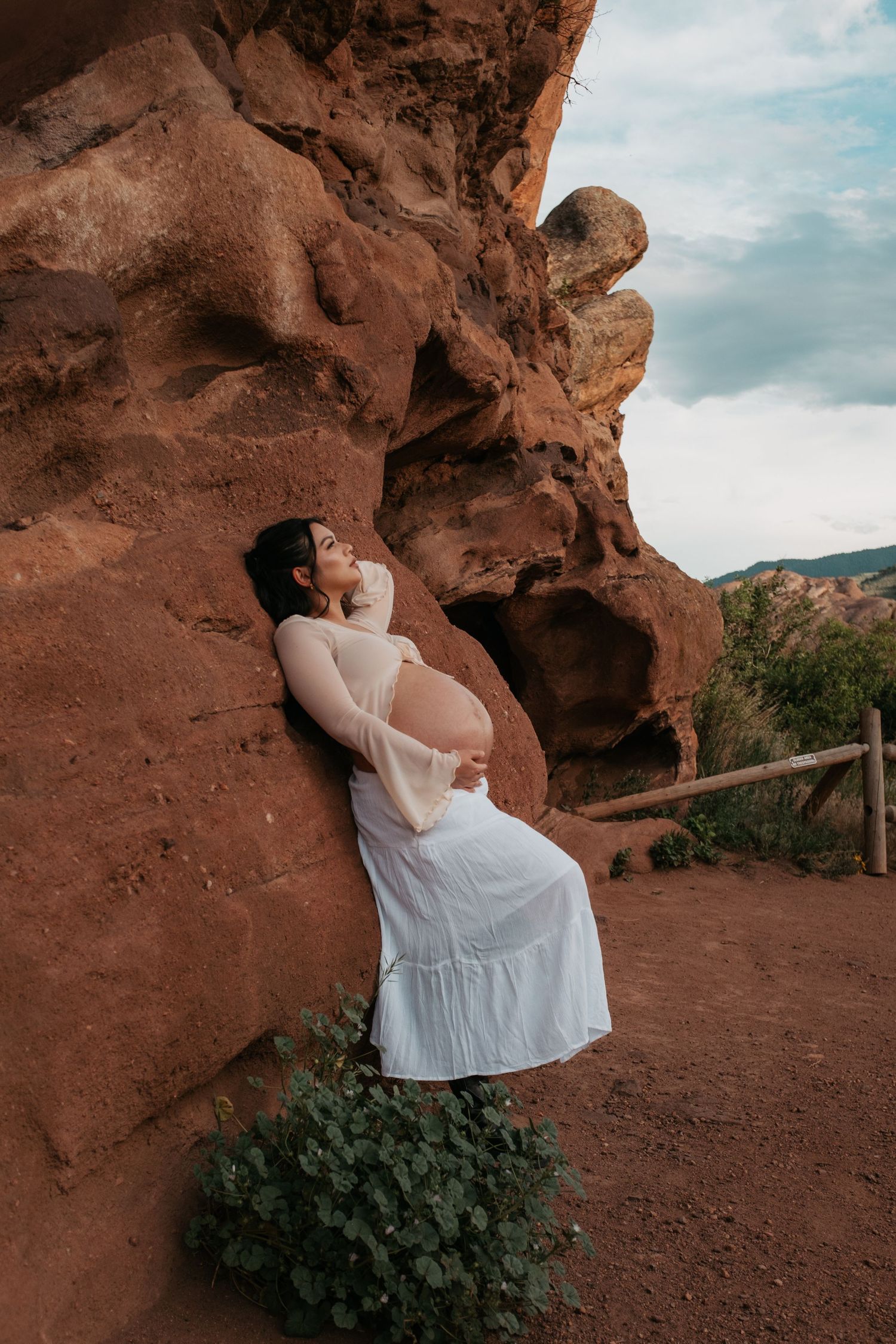 A dramatic maternity photo with someone posed against red rock formations in natural light.