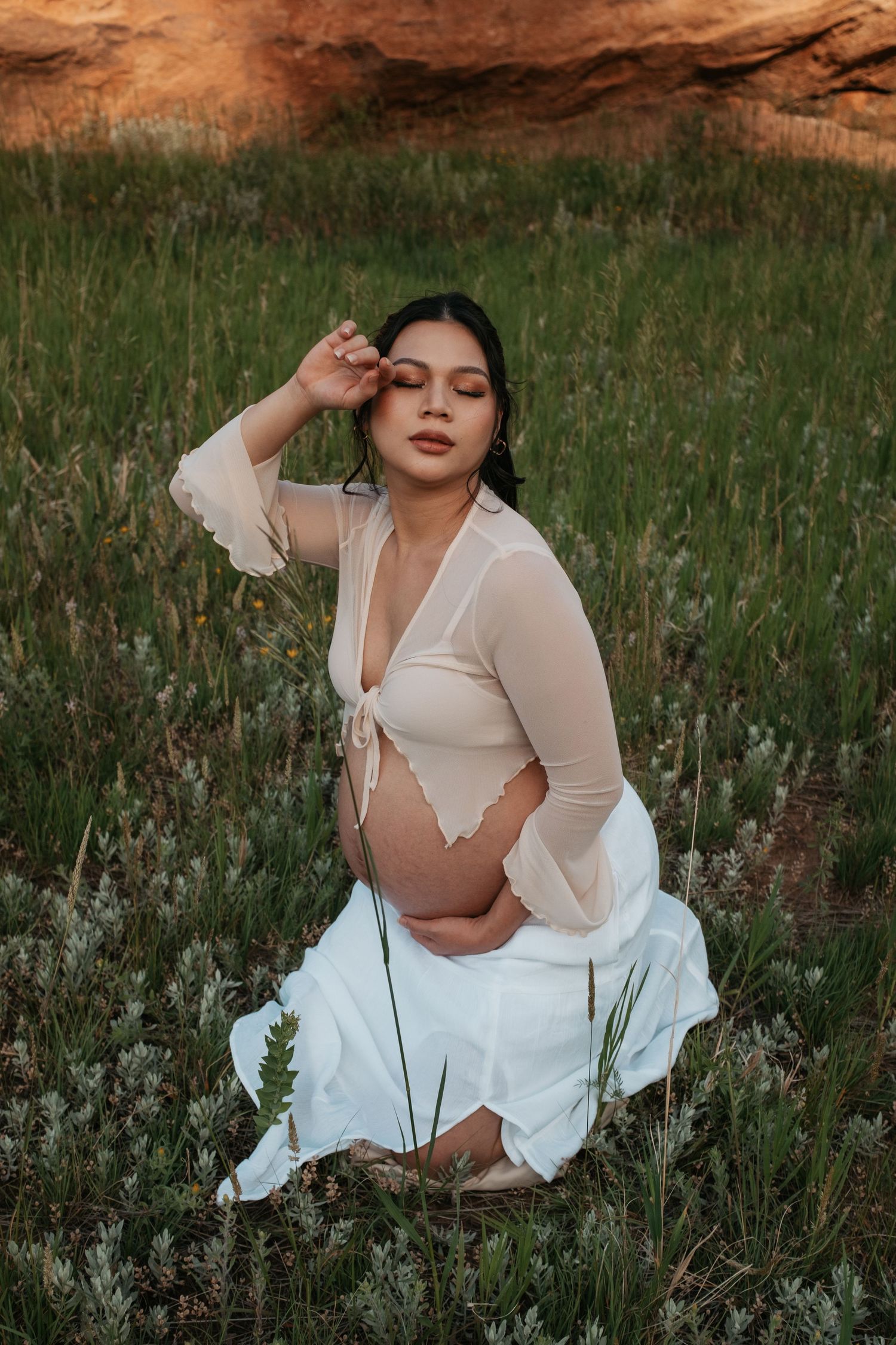 A dreamy maternity photo with someone in white against red rock formations and green grass.