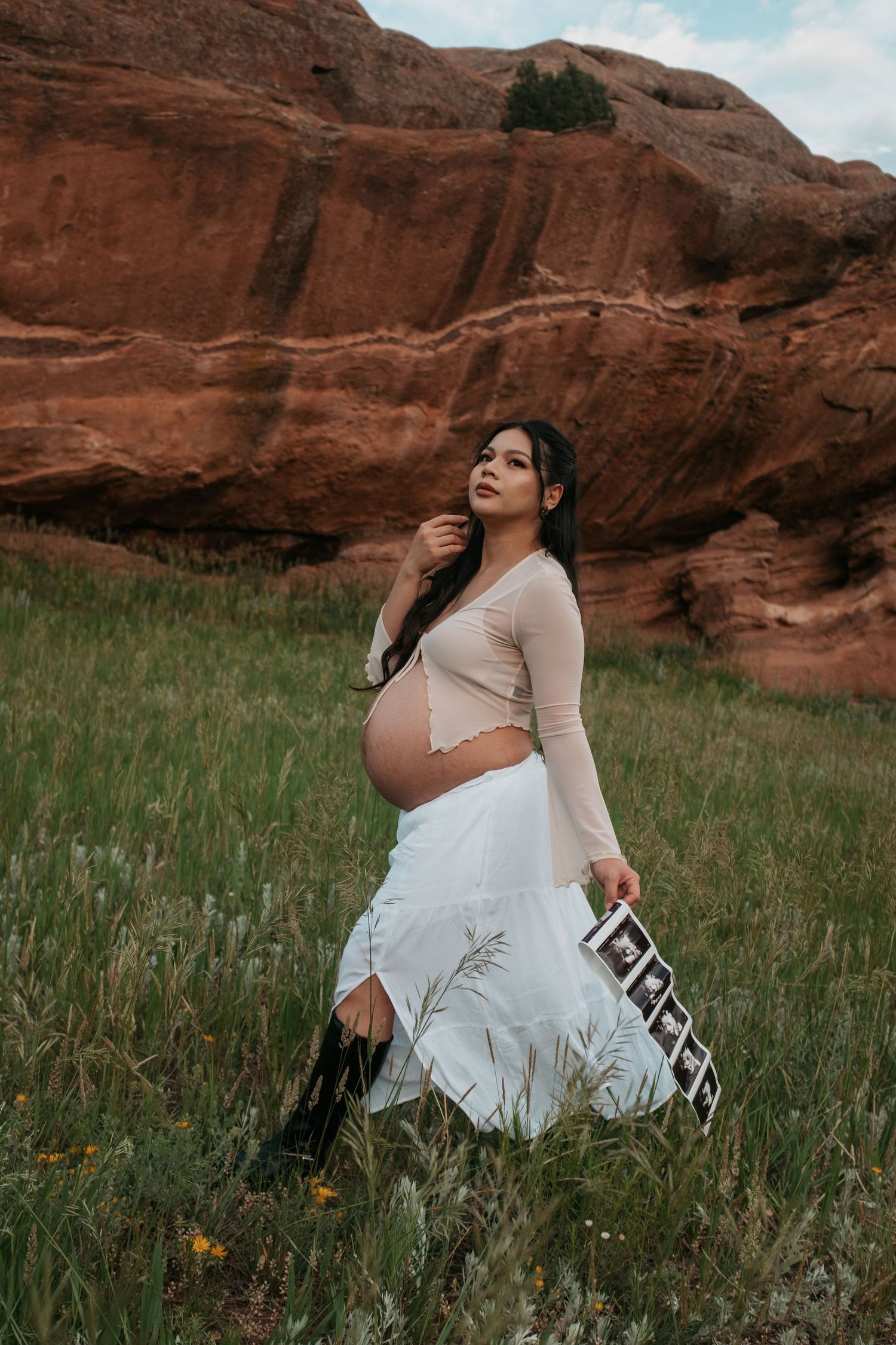 A maternity photoshoot in a scenic field against red rock formations with a flowing white dress.