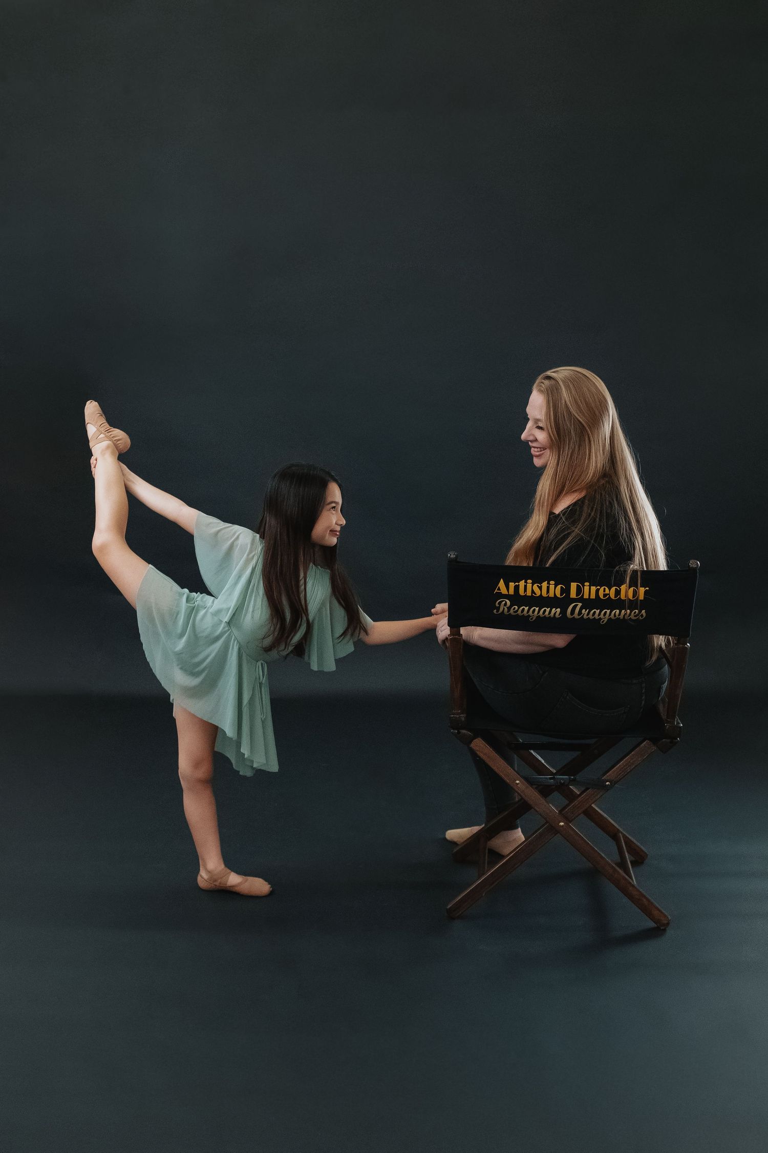 Ballet dancer strikes graceful poses while seated in an artistic director's chair against dark background.