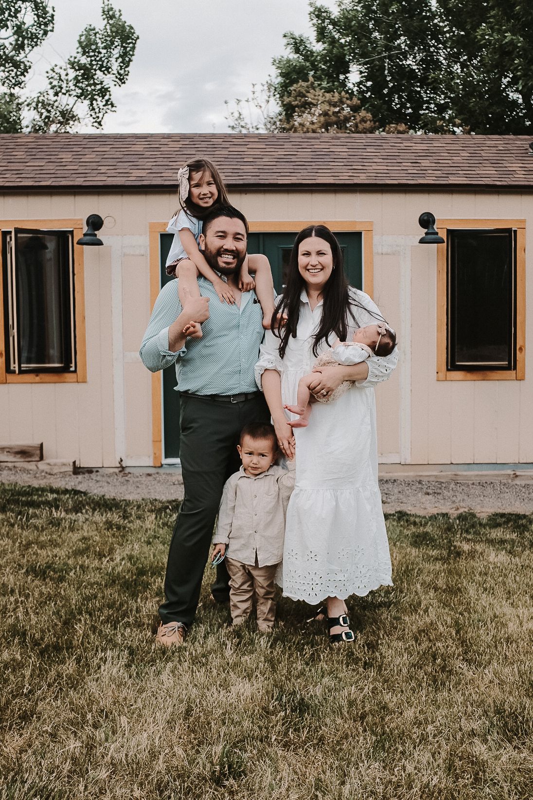 A family of five poses together outside their tan house with black-trimmed windows.