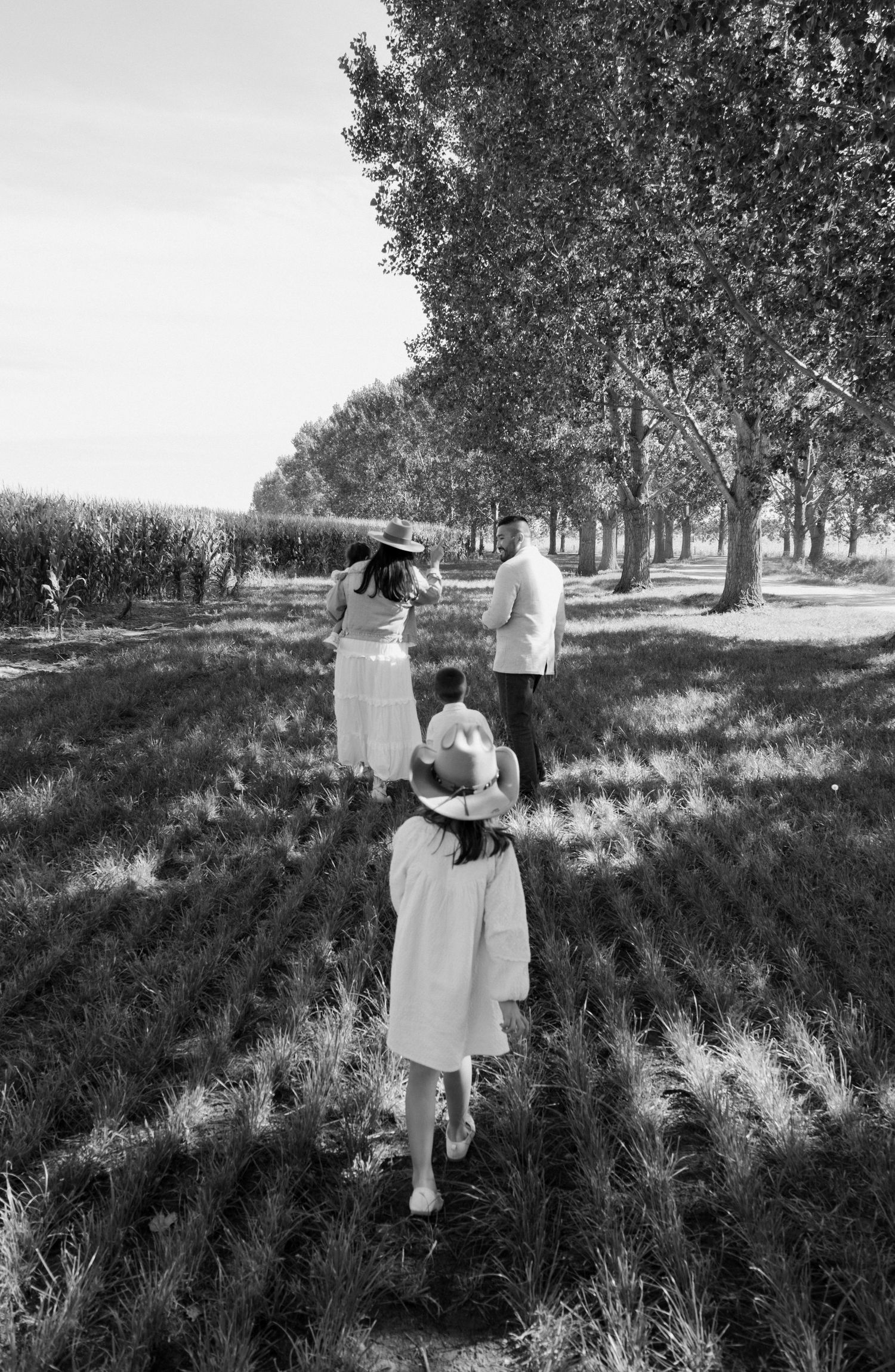 Black and white photo of a family walking through a field lined with trees on a sunny day.