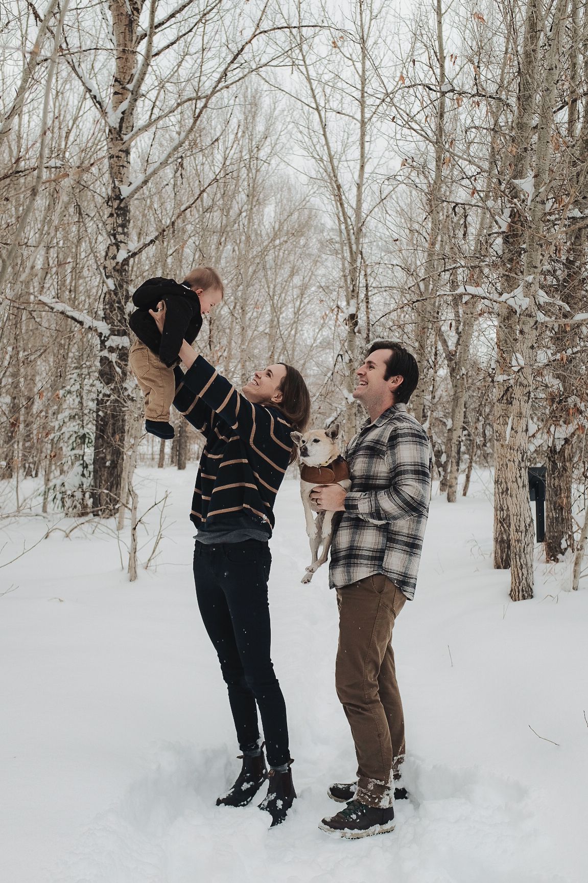 Two people playing with a child in a snowy birch forest during winter.