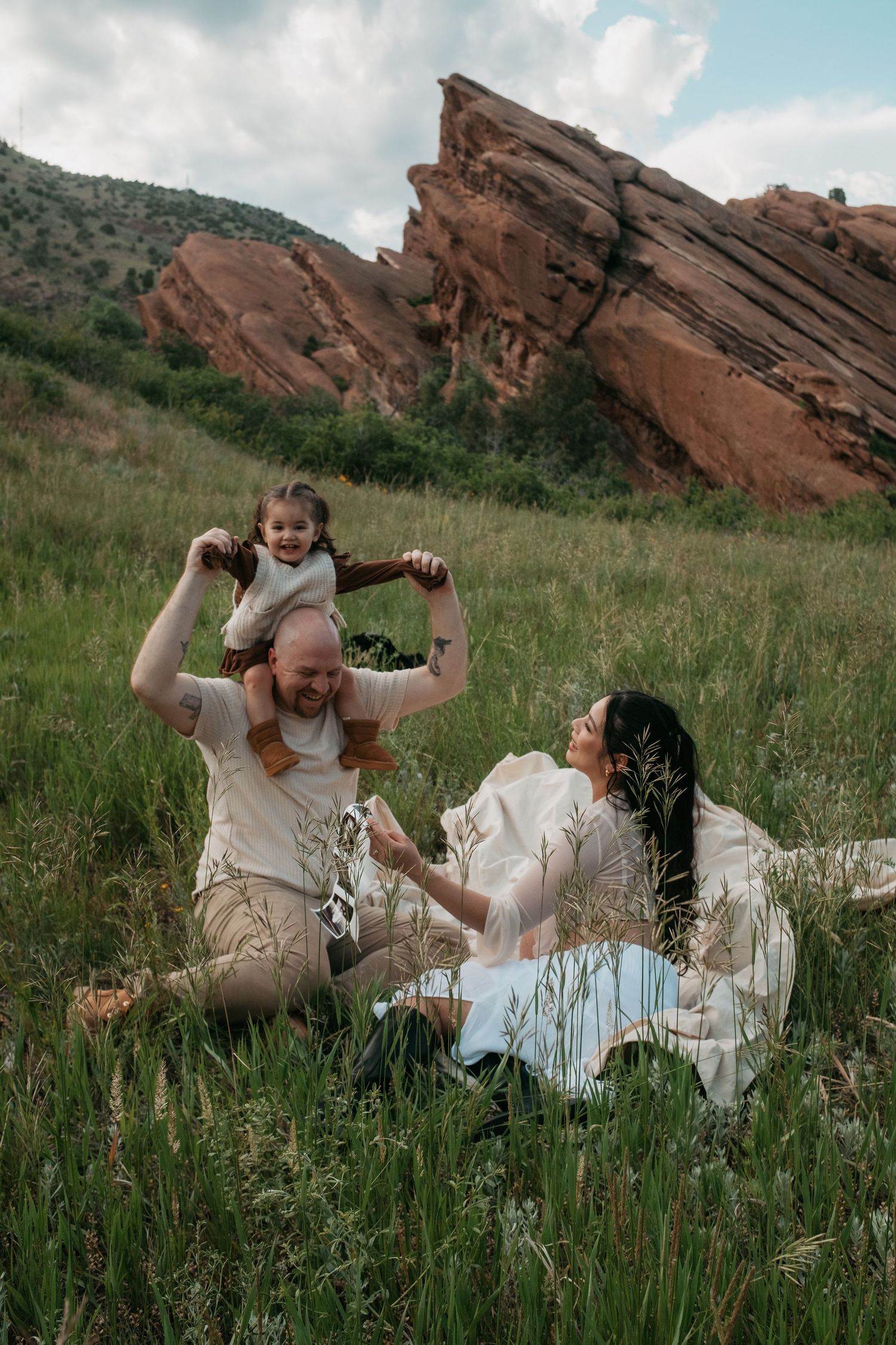 Happy family playing in grassy field with stunning rock formations in background.