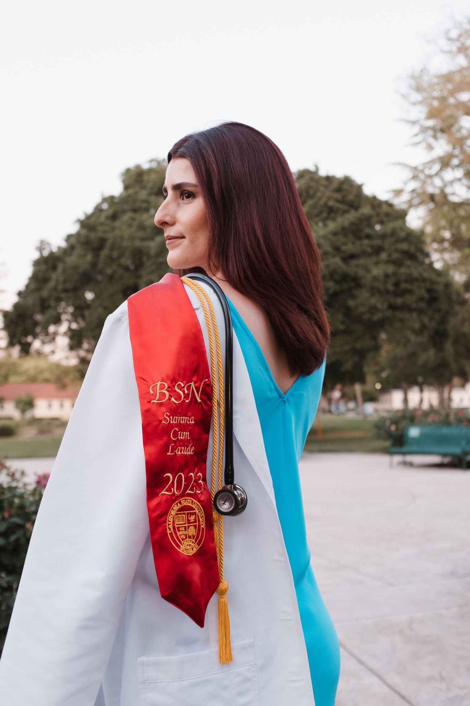 Graduate wearing a red and white graduation stole against a blurred outdoor background.
