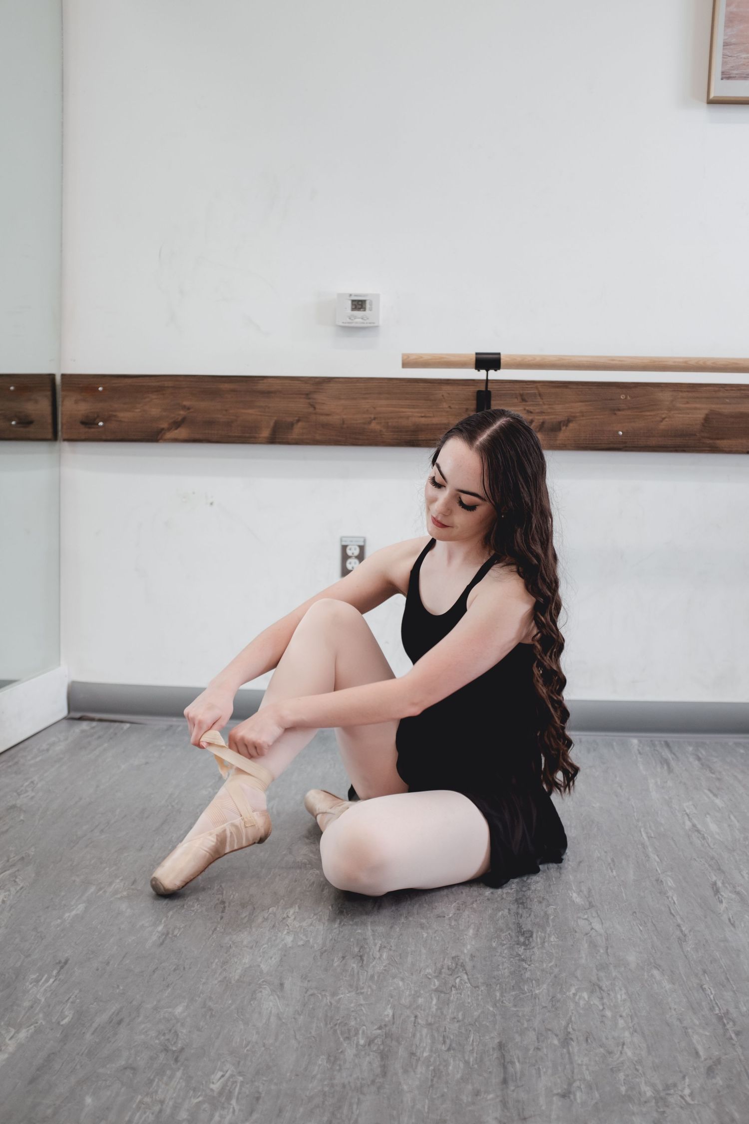 Dancer adjusts ballet shoes while sitting on studio floor.