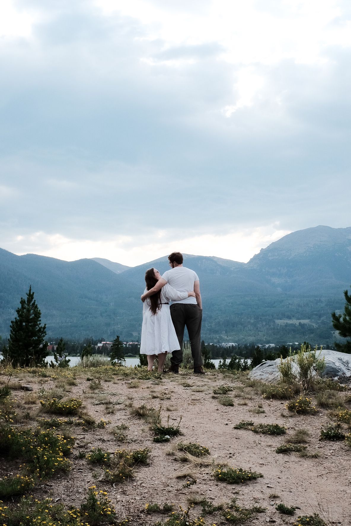 Couple stands on mountain overlook viewing dramatic landscape and cloudy sky.