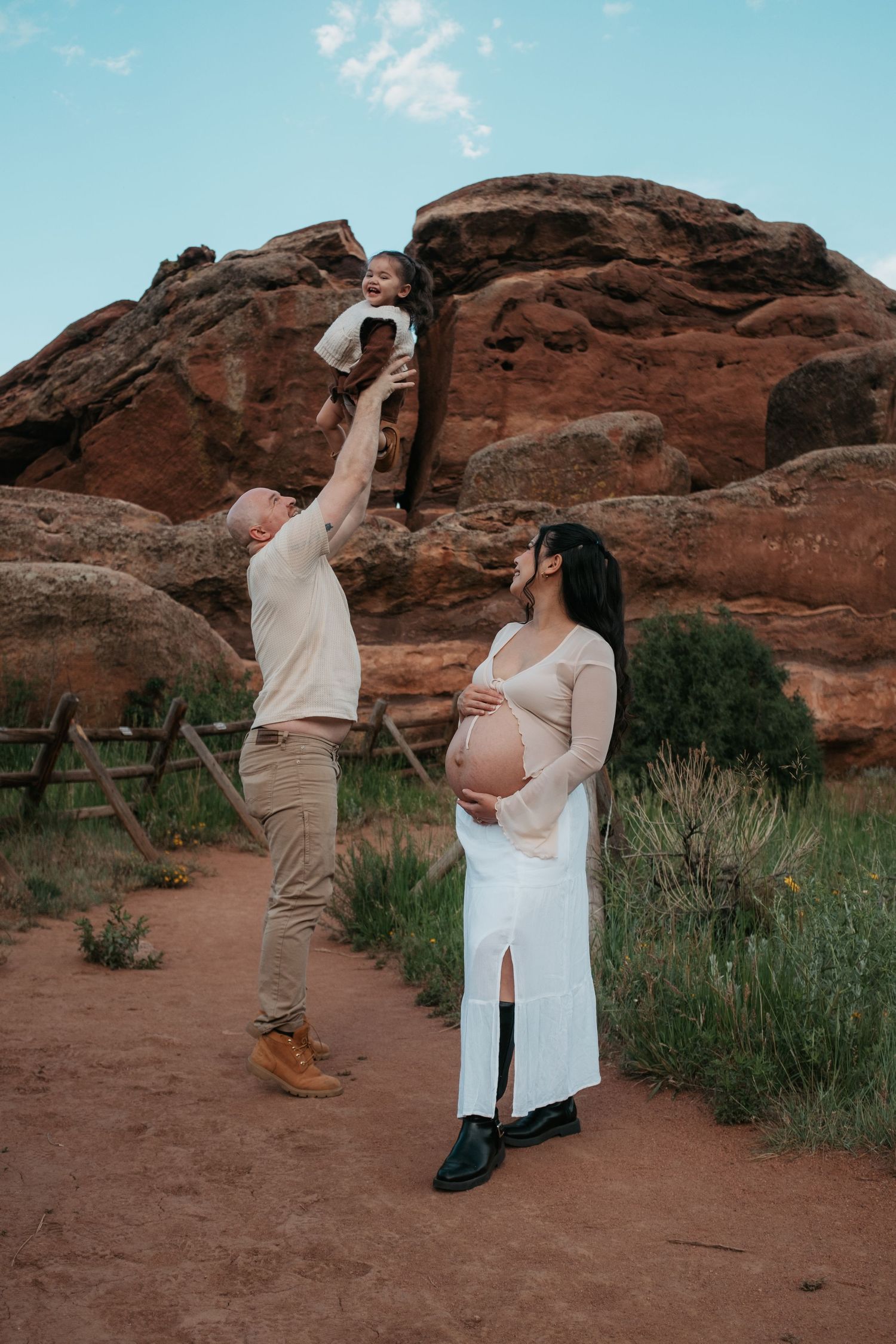 Playful pregnancy announcement photoshoot with couple dancing in front of red rocks.