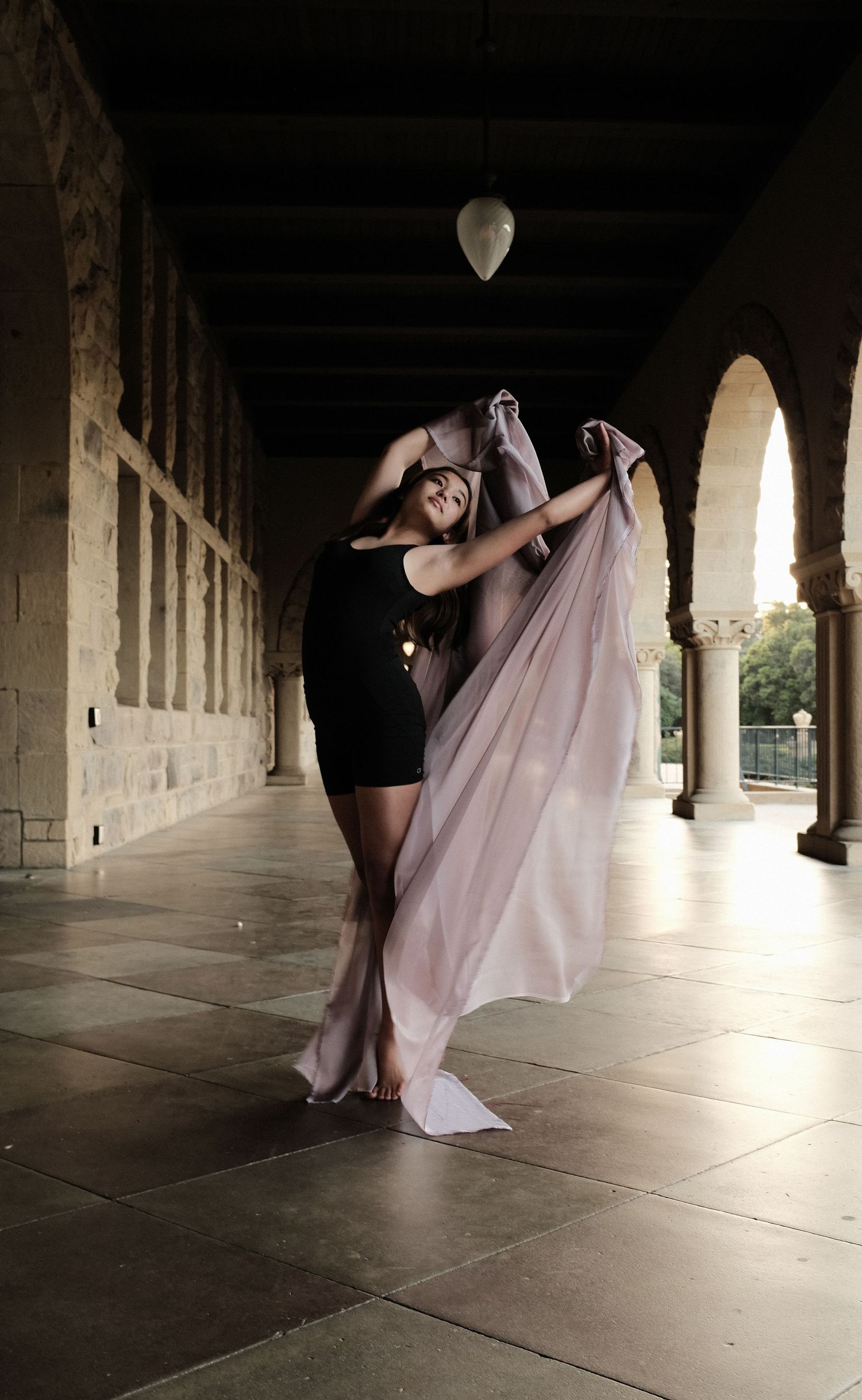 Modern dance performance sequence under dramatic columned archway shows flowing pink fabric movements in dark lighting.