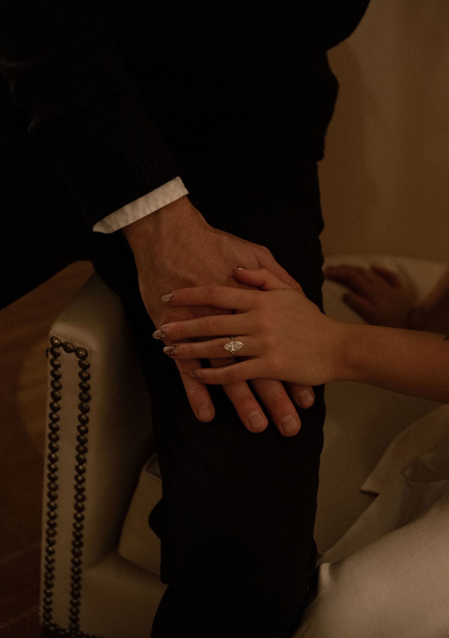 Close-up of hands with an engagement ring, a couple sharing a tender moment in formal attire.