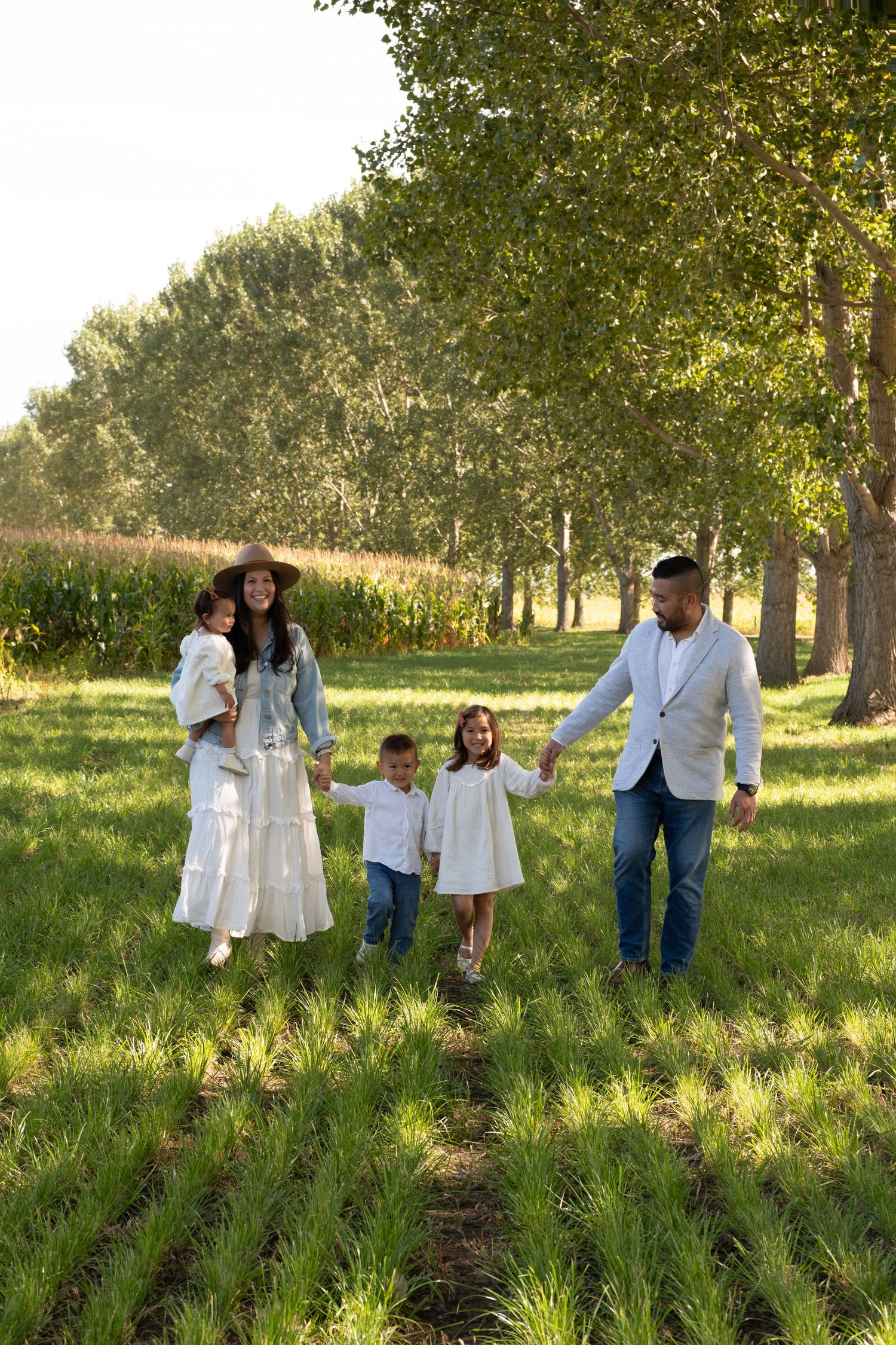 Happy family of five walking through lush green fields surrounded by tall trees on a sunny day.