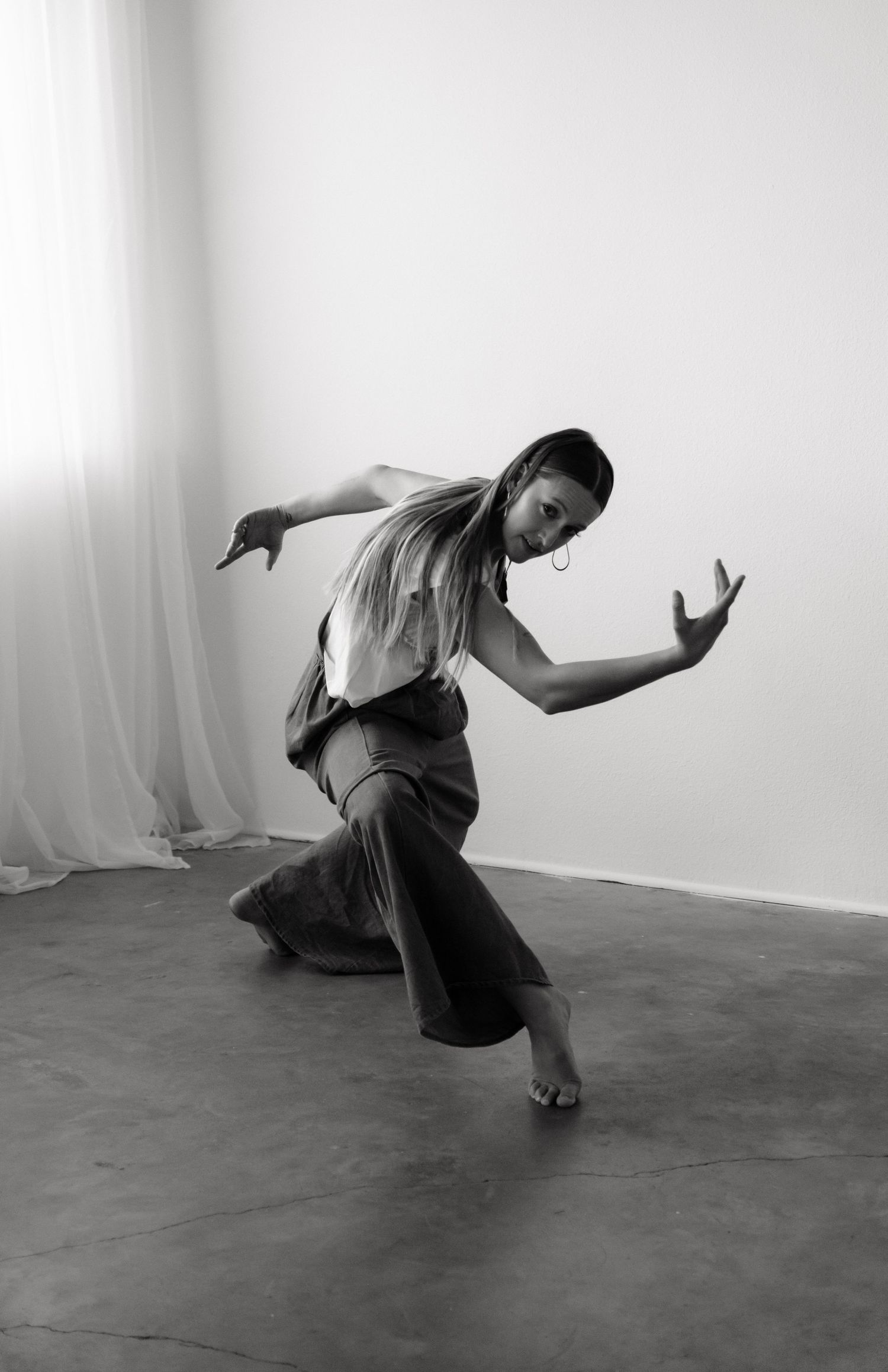 Black and white photo of a barefoot dancer in dynamic pose, wearing wide-leg pants and top in a studio.