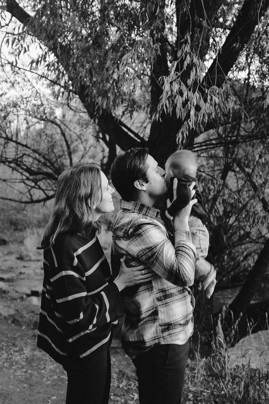 Black and white photo of three people looking up at trees together.