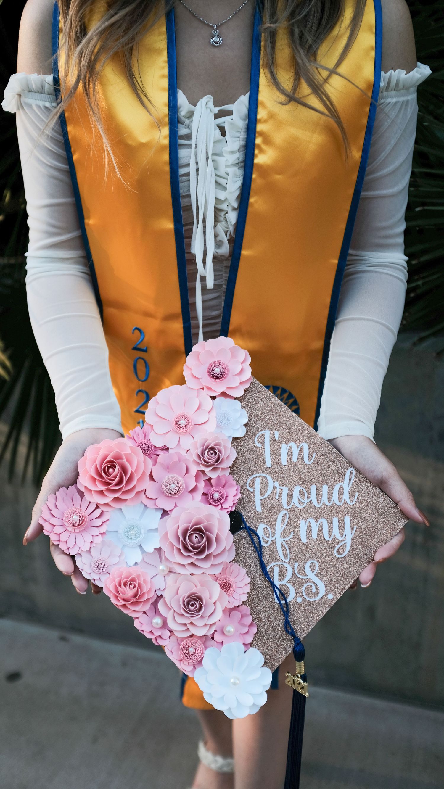 A graduation cap decorated with pink and white paper flowers and text reading 'I'm Proud of my BS'.