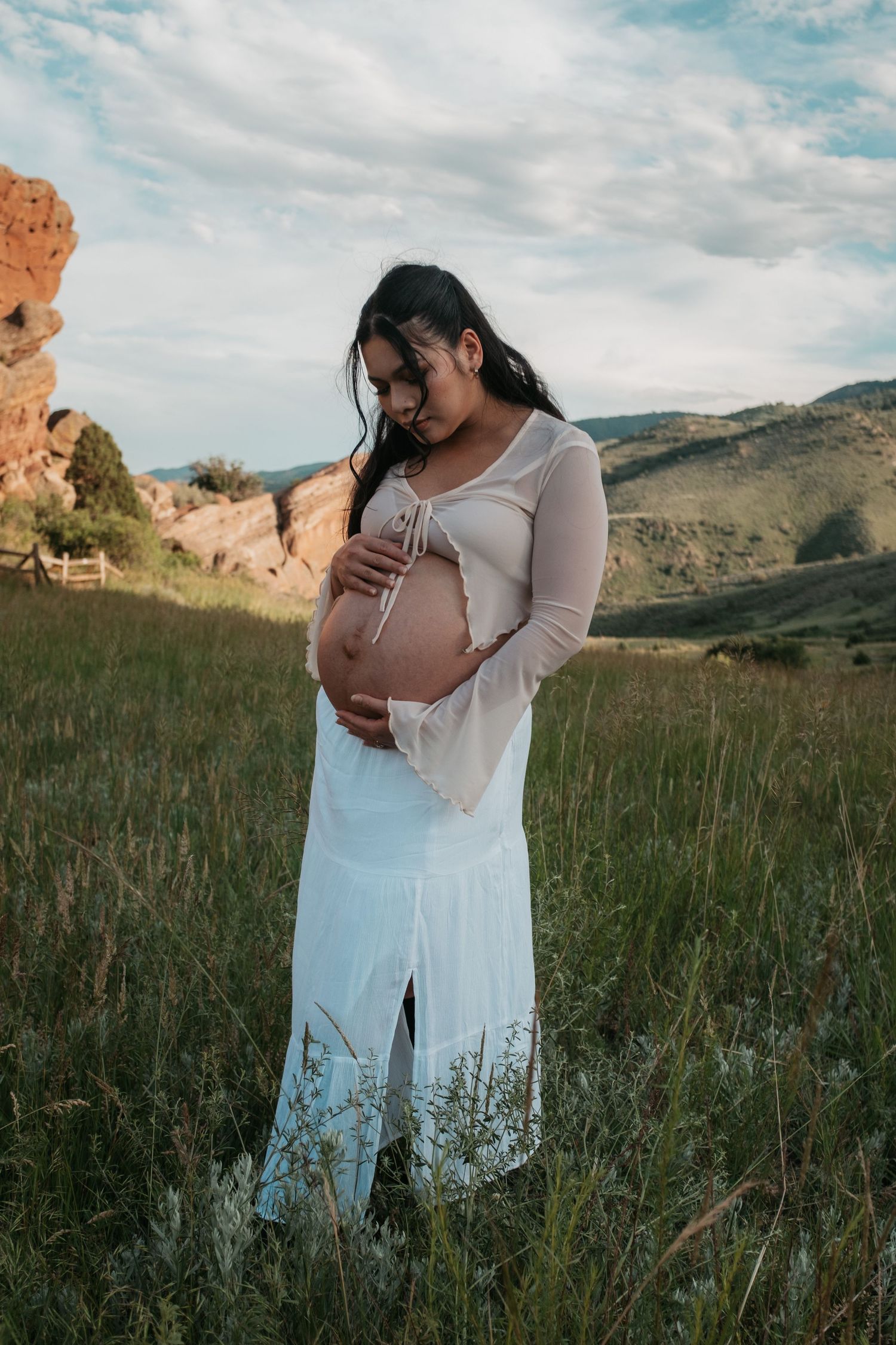 Intimate maternity moment captured in mountain meadow with red rocks in background.