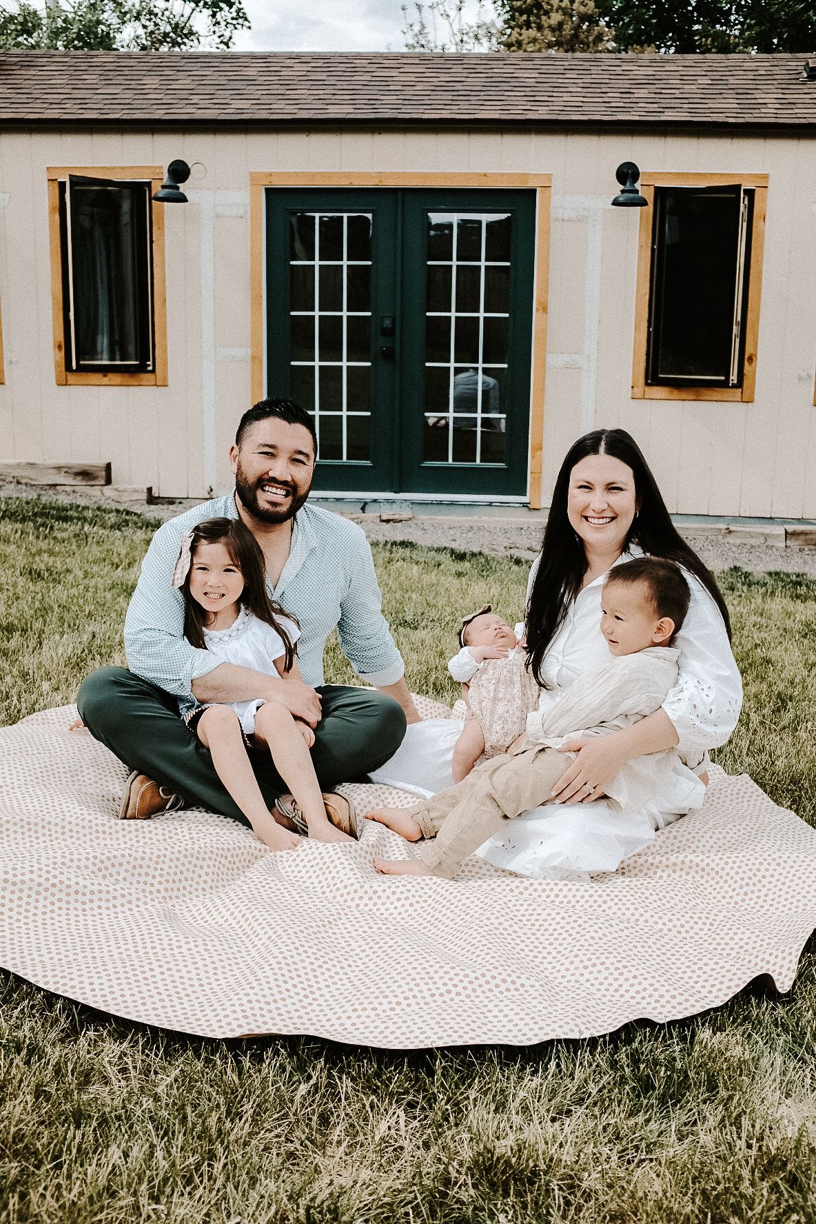 Family sitting together on a blanket in front of a charming cottage with French doors.