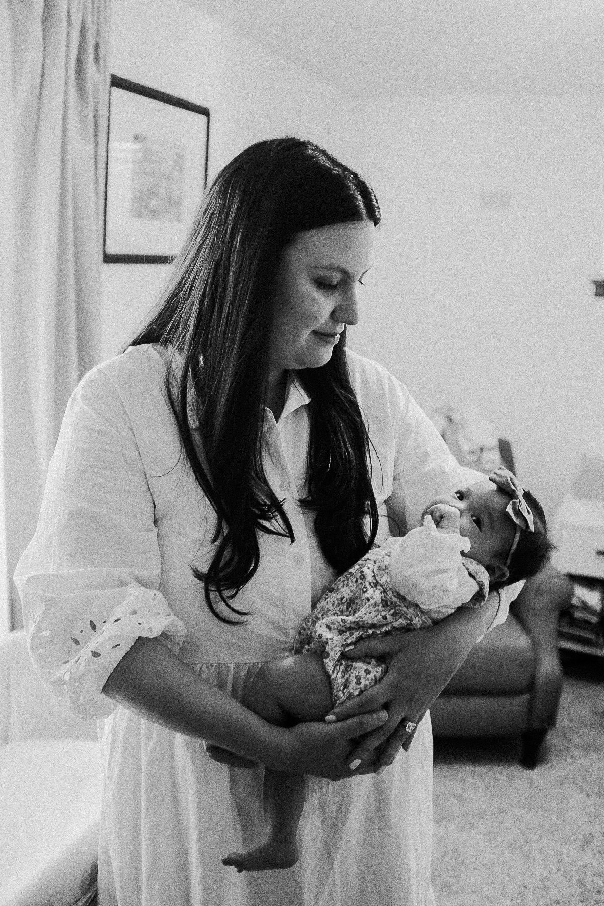 Black and white portrait of mother tenderly holding newborn baby in home setting.