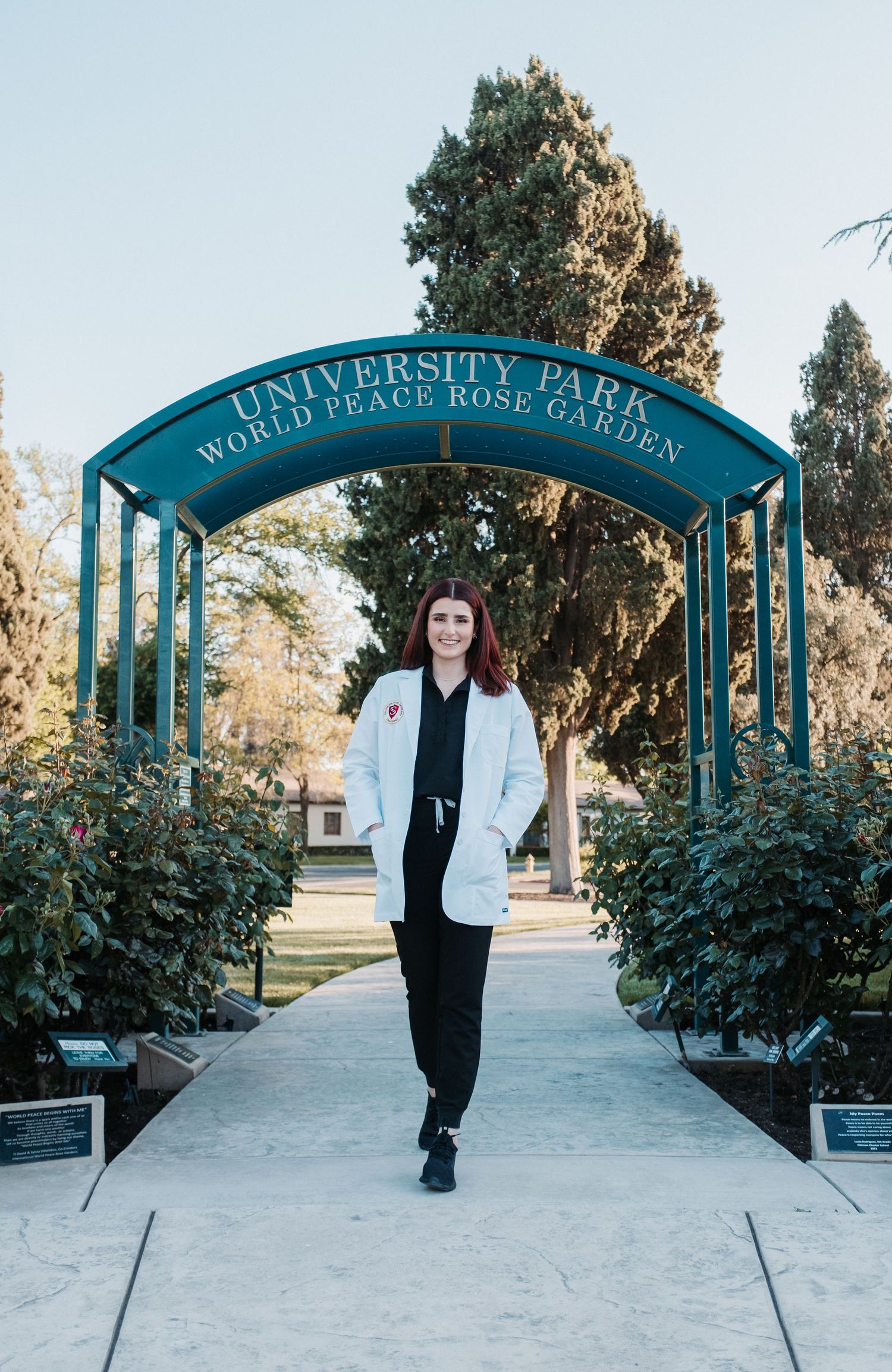 Graduate walking under University Park World Peace Rose Garden archway.