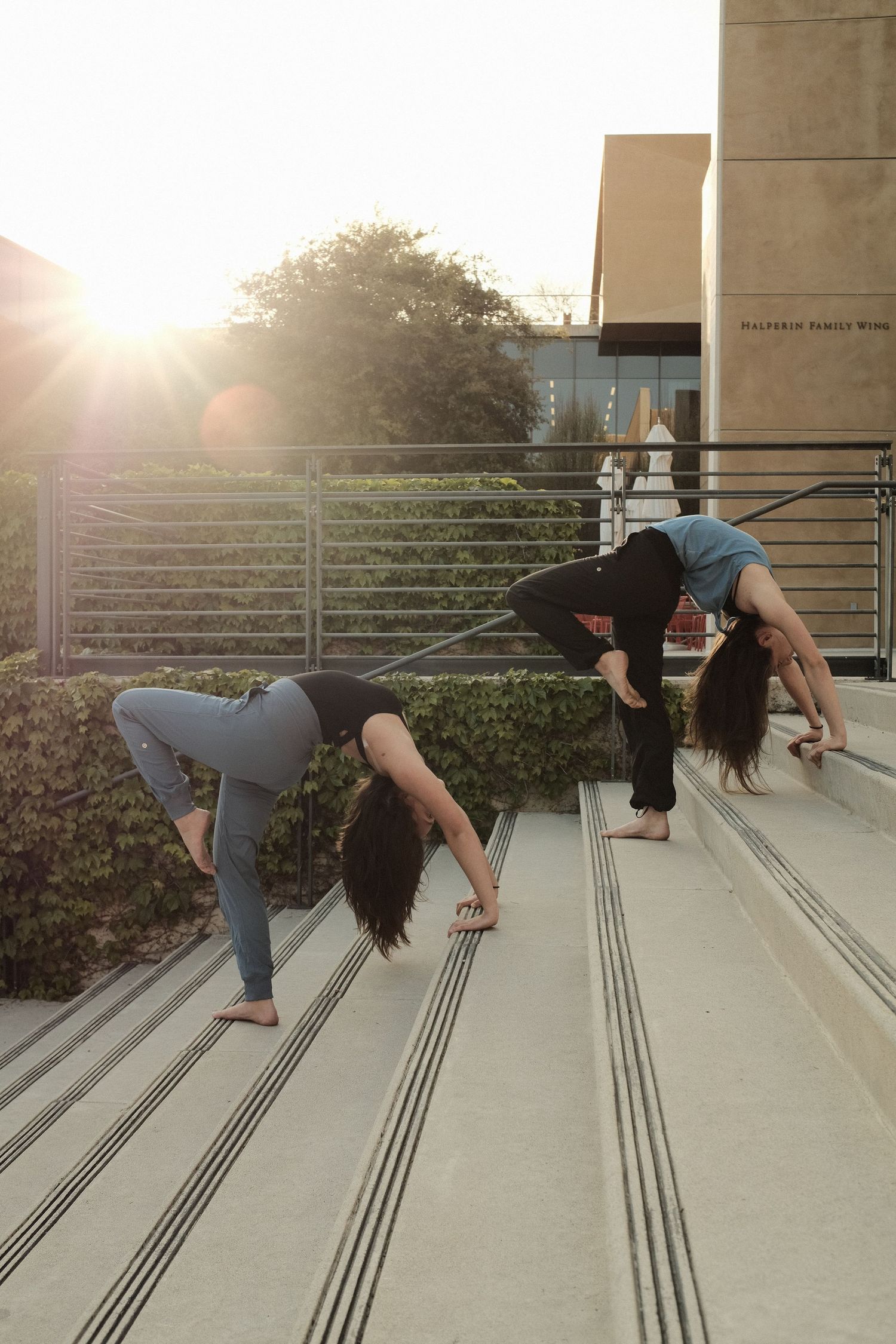Two dancers perform modern dance movements on concrete steps at sunset.