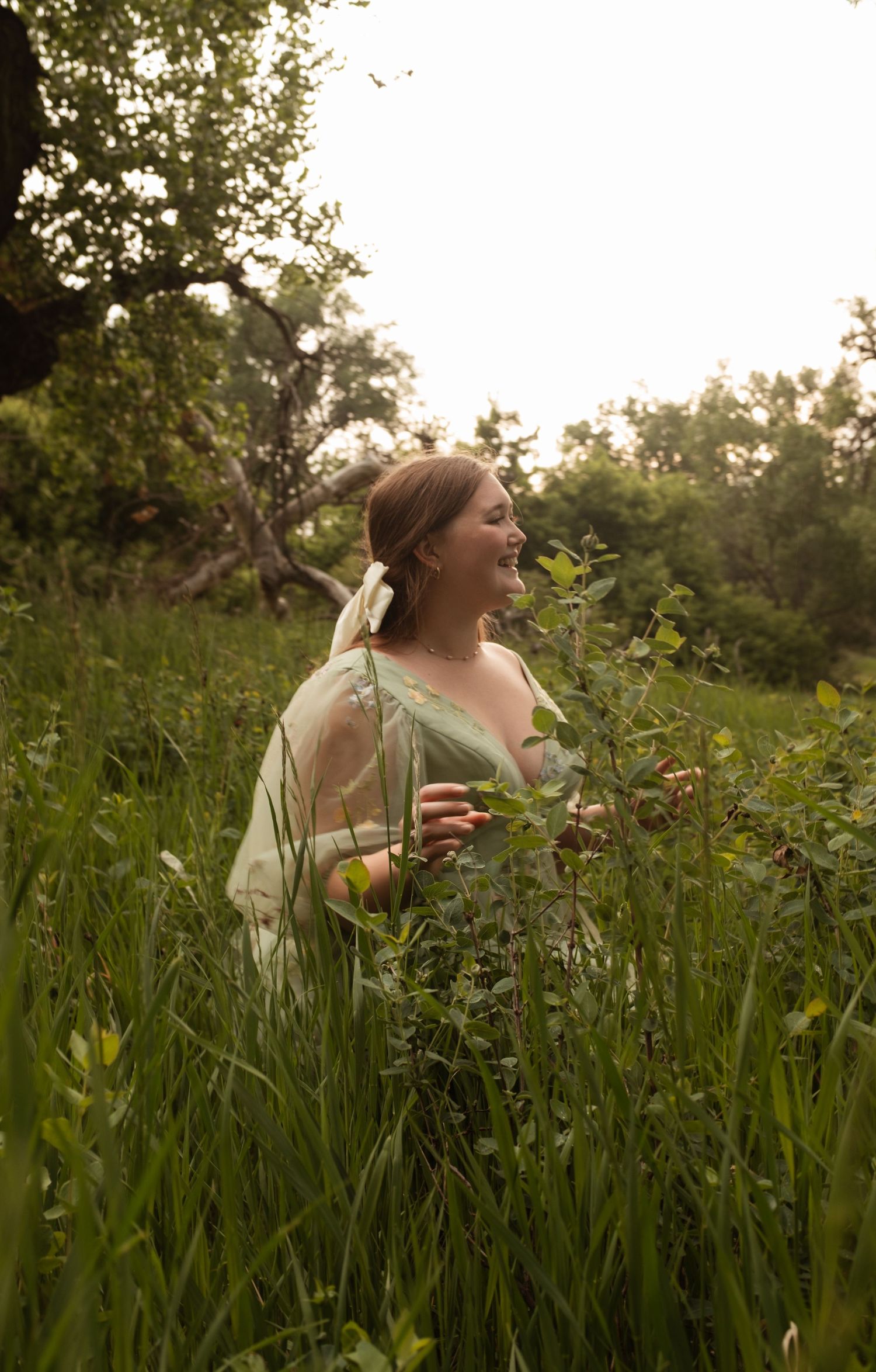 Figure in vintage-style dress stands among wildflowers in sunlit meadow.