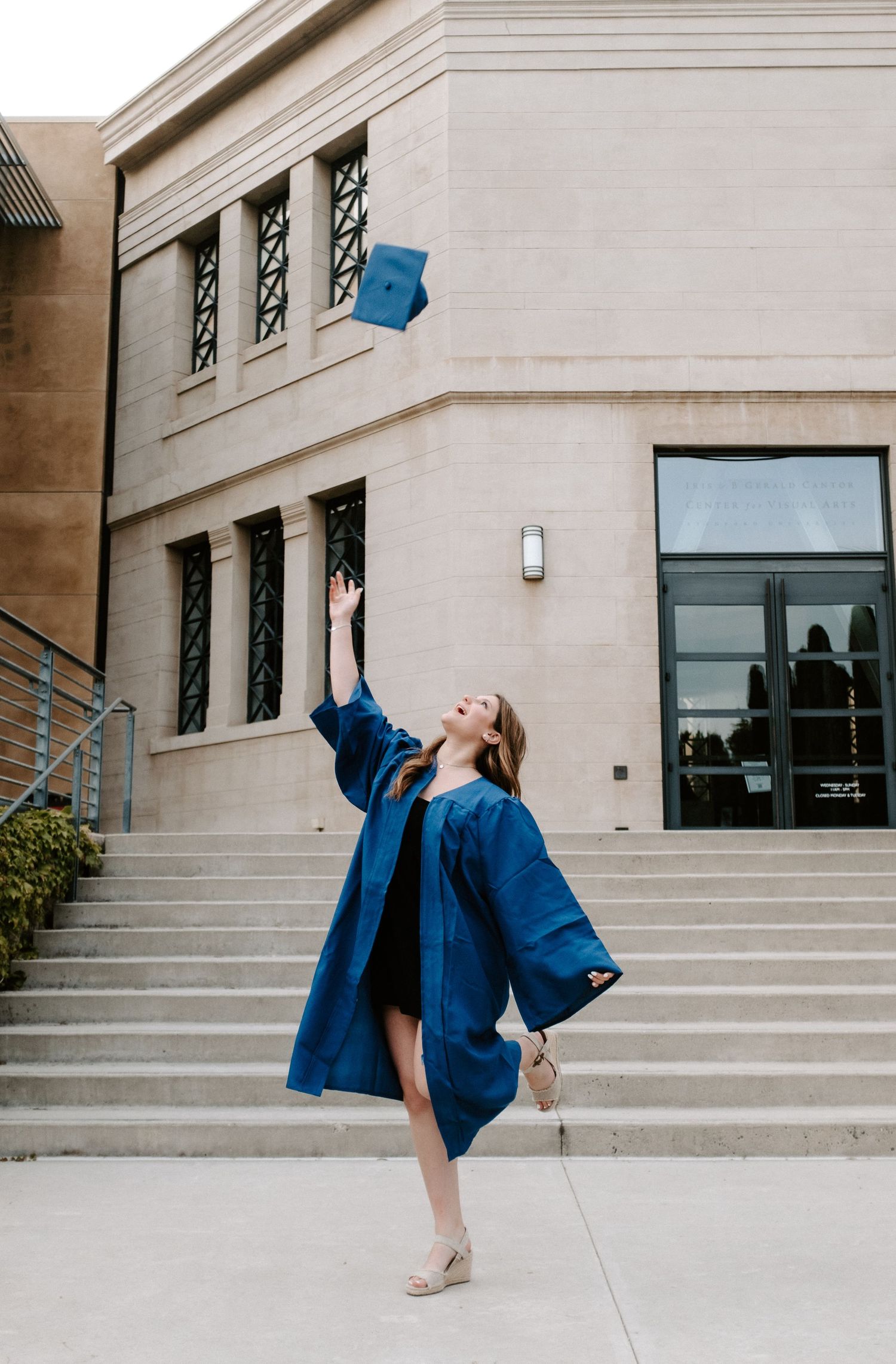 Celebratory graduation poses on concrete steps in front of modern building facade.
