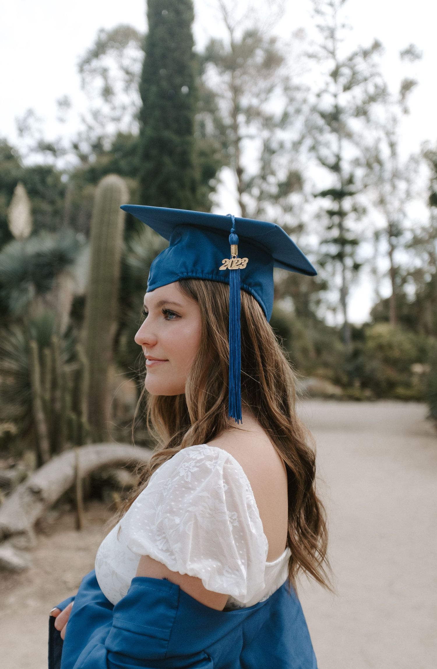 Graduation photoshoot in a desert garden featuring blue academic regalia and white lace dress.