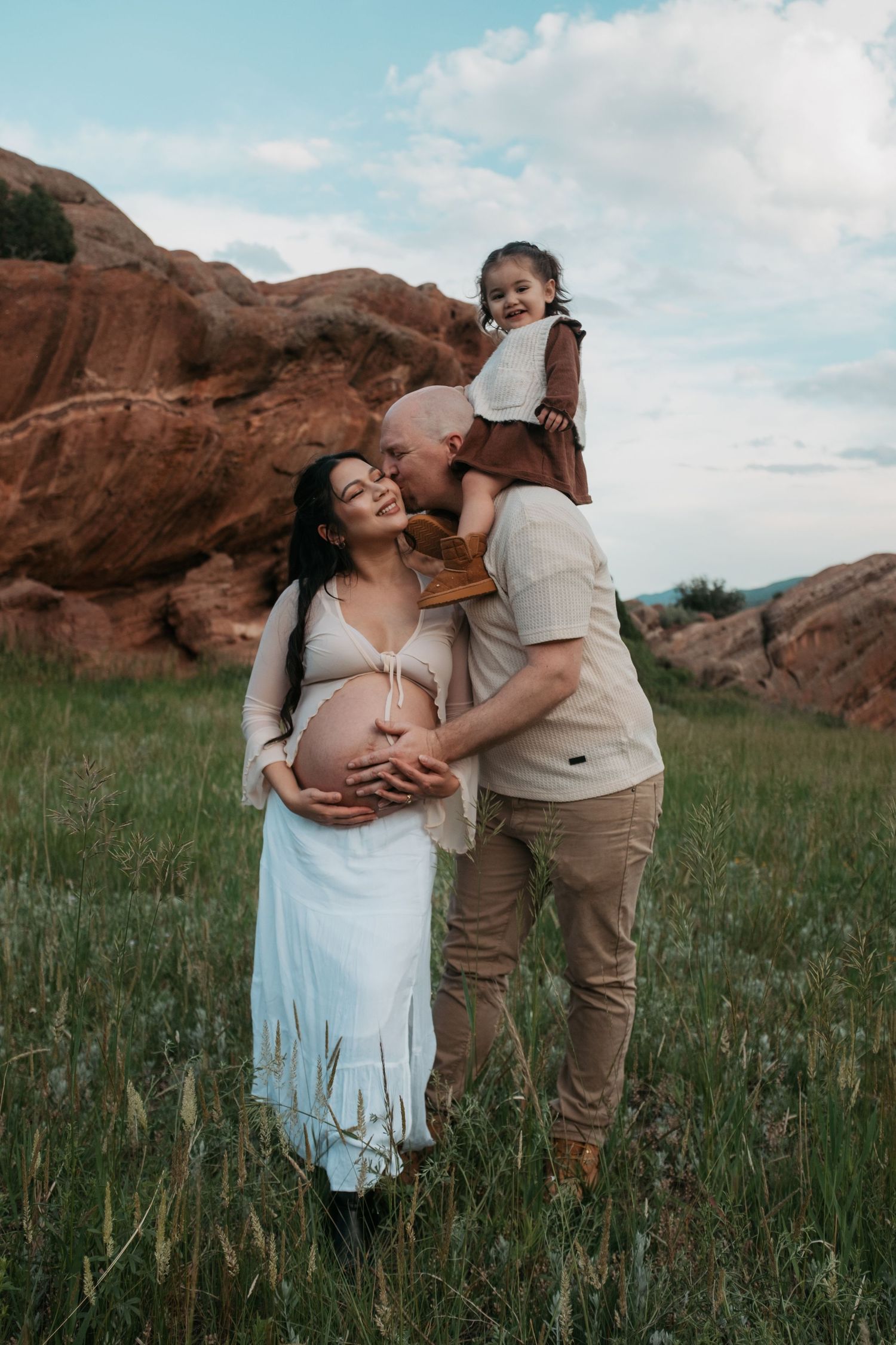 A touching maternity photo captured against red rocks and blue sky in a grassy field.