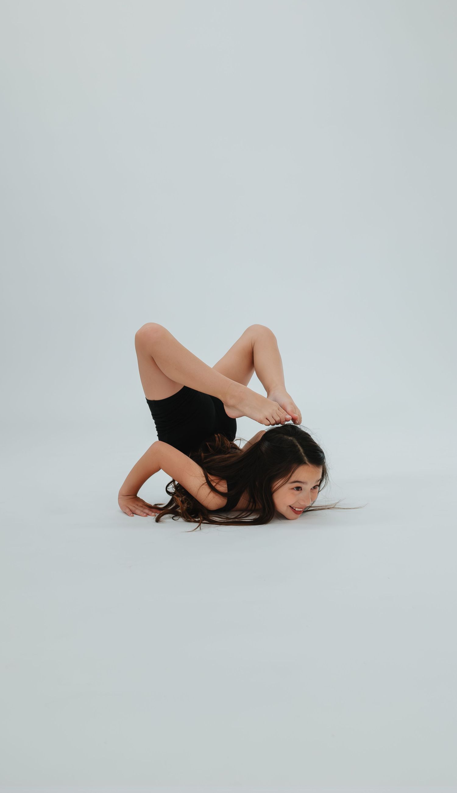 Modern dancer performs contemporary floor movement in black leotard against white background.