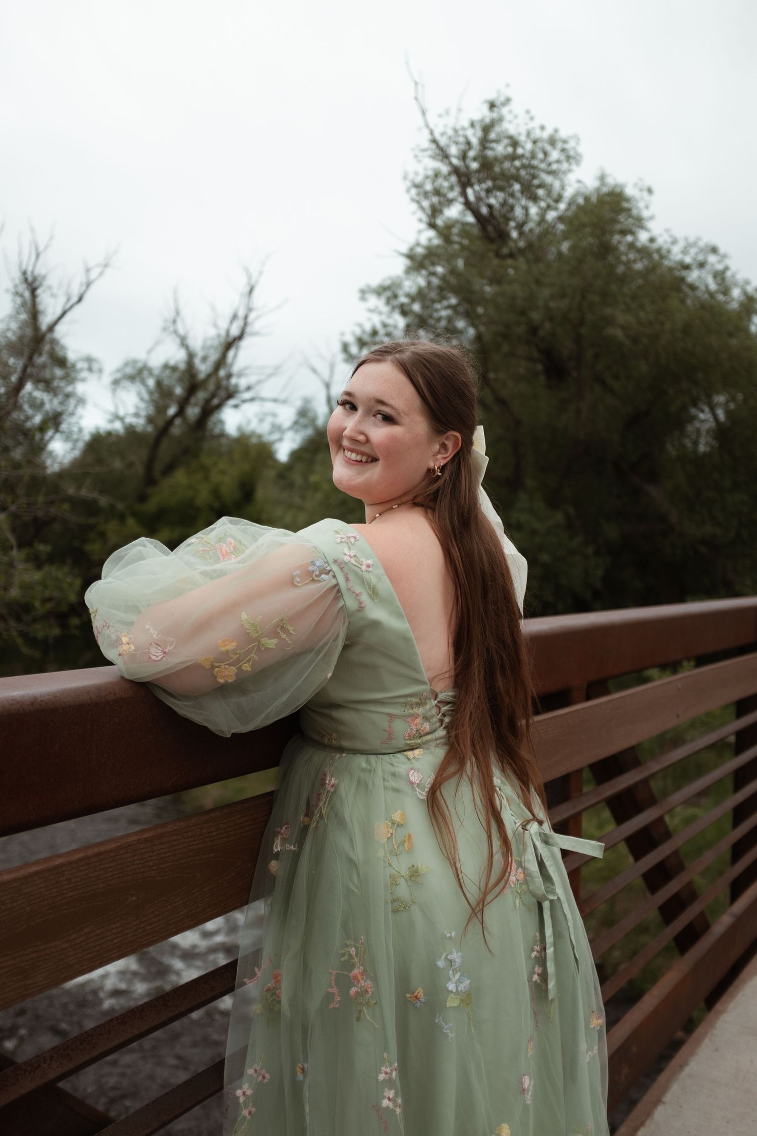 Woman in mint green vintage dress poses on bridge with flowing sleeves.